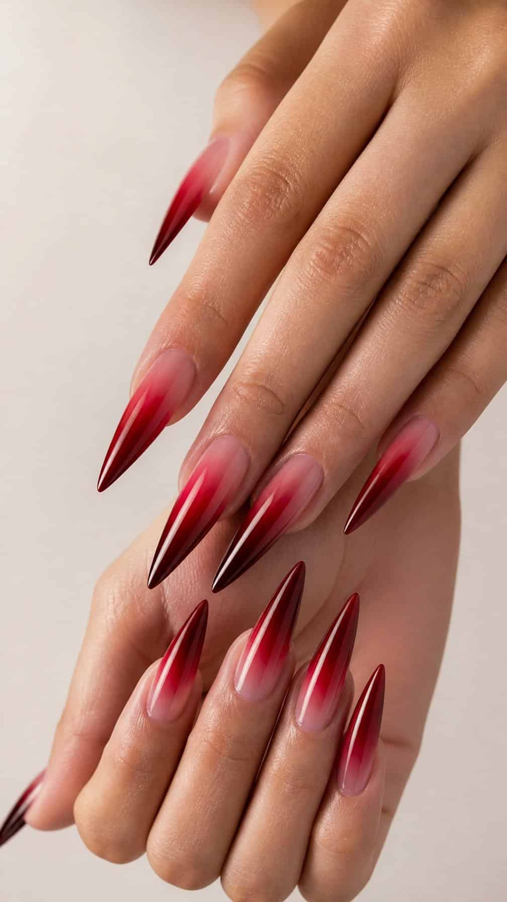 Close-up of hands displaying long red ombre stiletto-shaped nails.