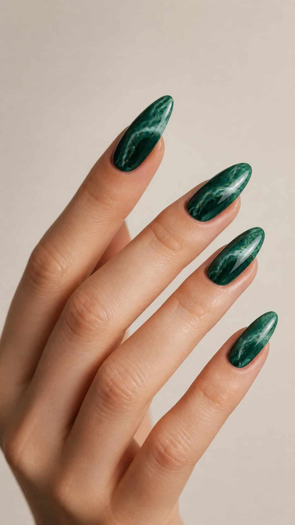A hand with long emerald green marble almond-shaped nails against a neutral background.