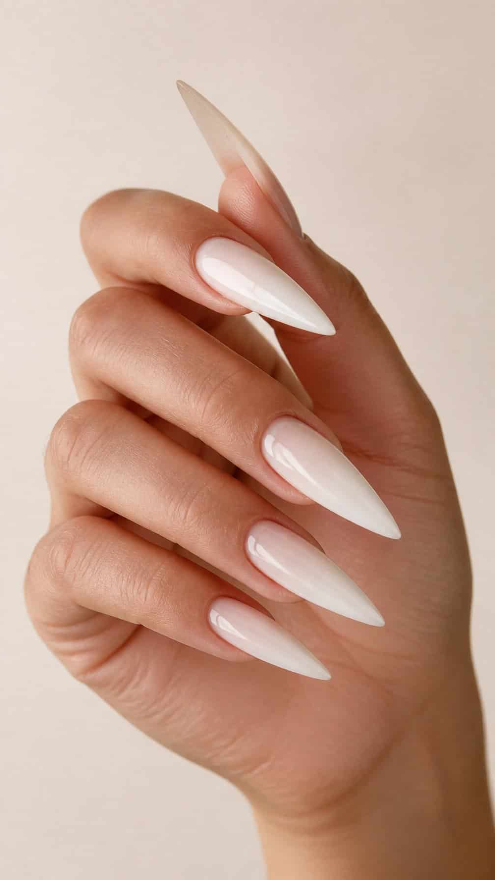 A hand with long, glossy milky white stiletto-shaped nails.