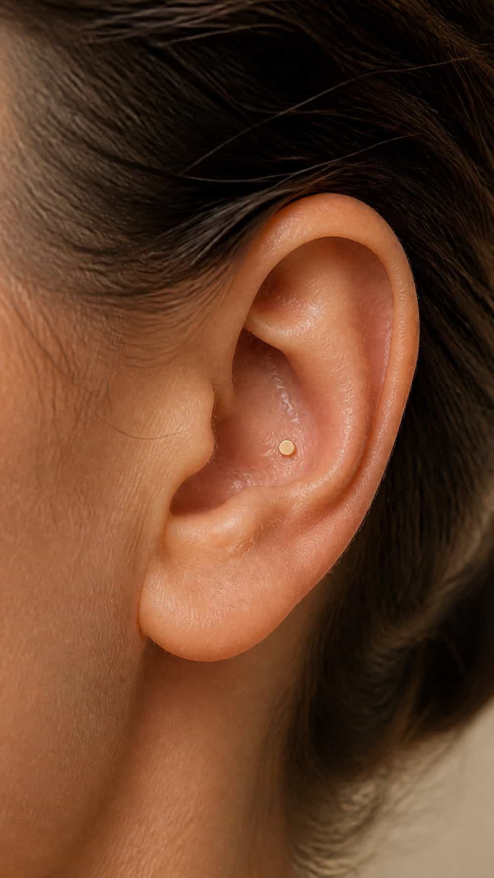 Close-up of an ear wearing a small gold disc conch piercing.