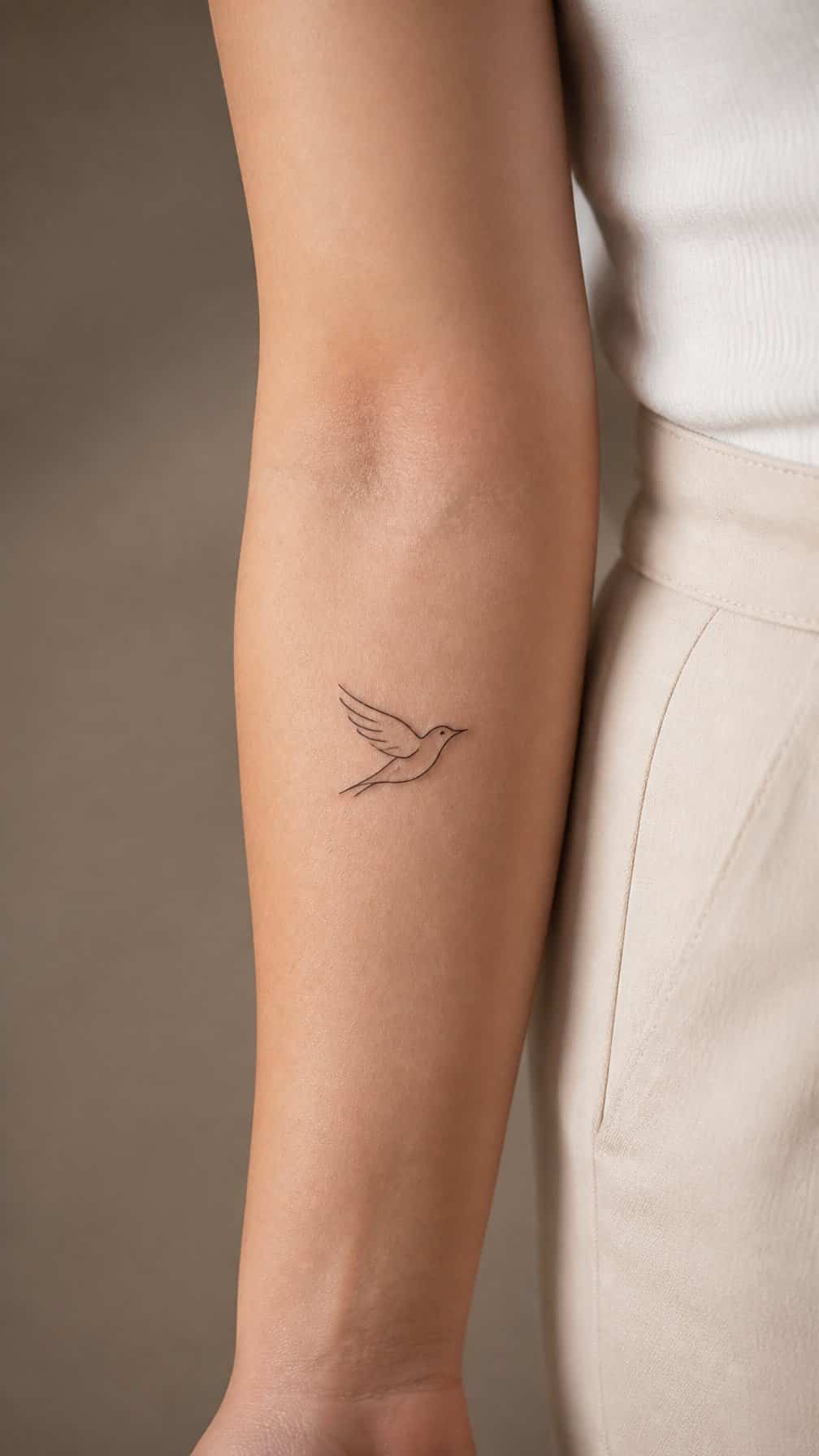 A small bird tattoo in flight on a person’s inner forearm.