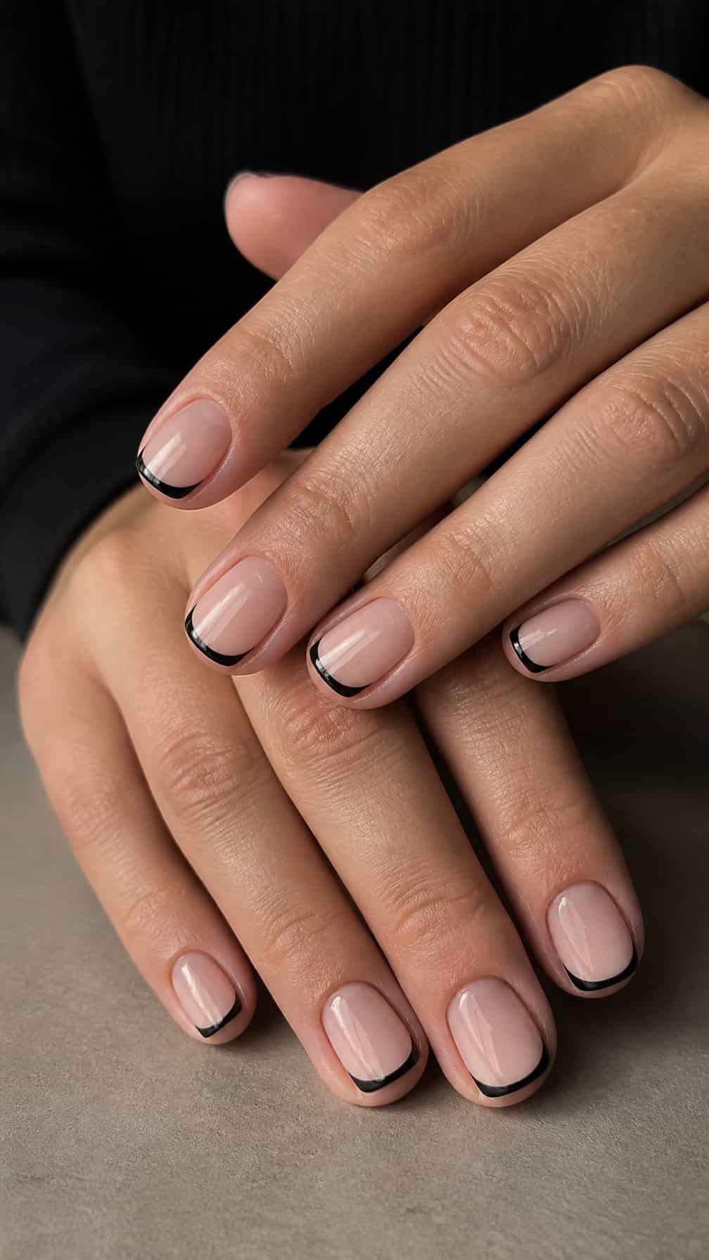 A close-up of hands with short nails painted with thin black French tips.