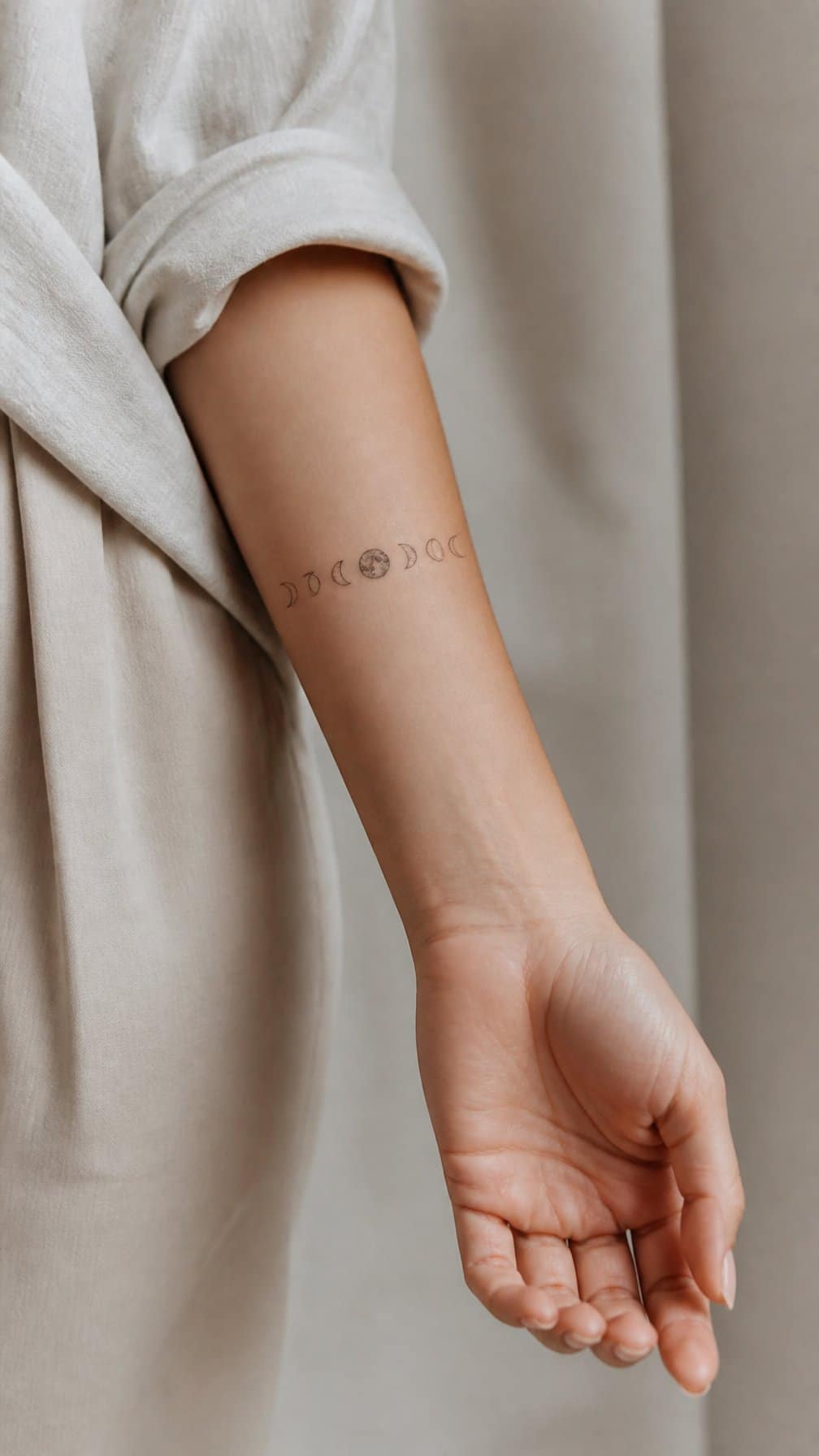 A woman's forearm with a delicate minimalist tattoo showing the phases of the moon.