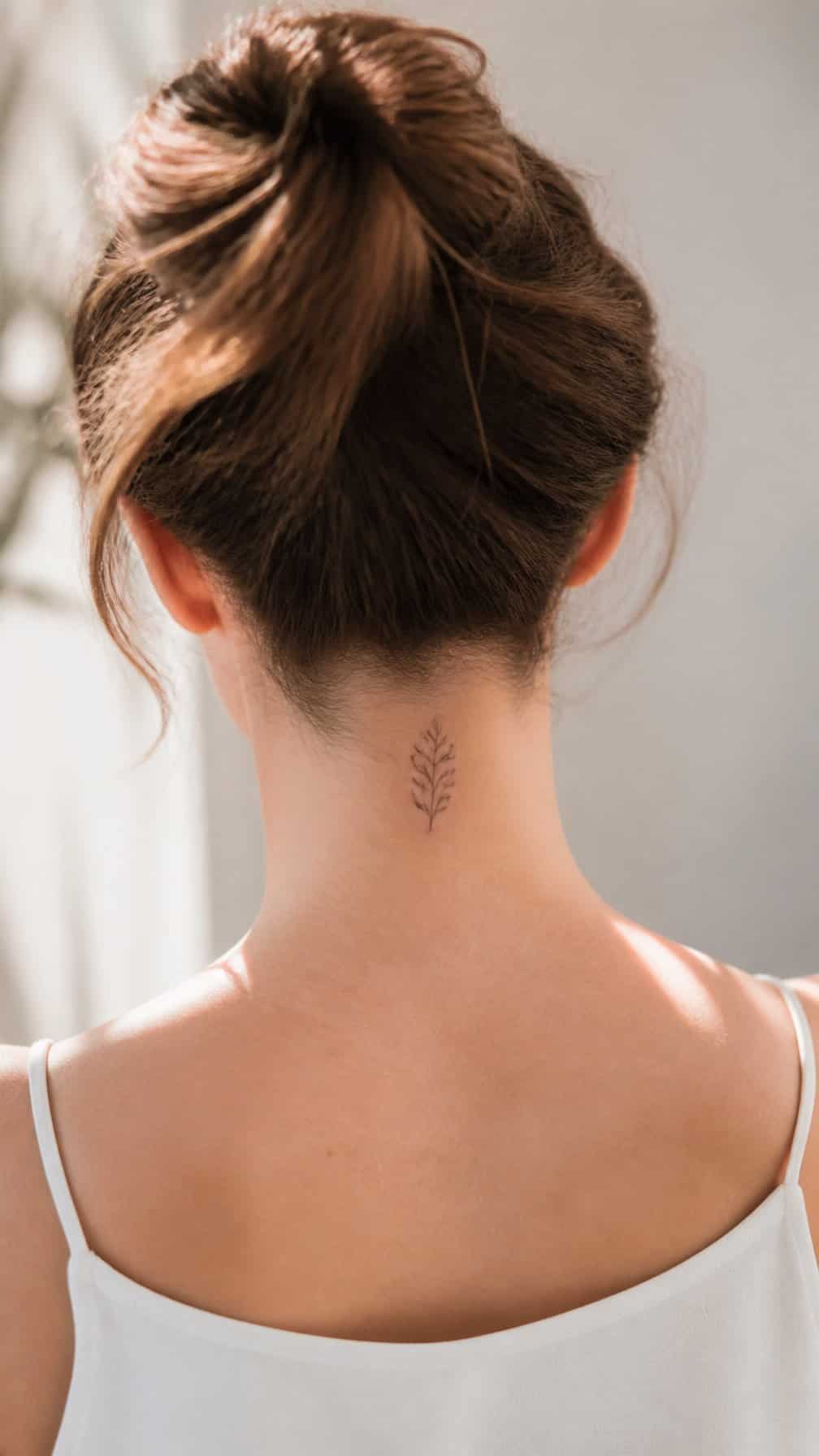The back of a woman’s neck with a small delicate tattoo at the nape.