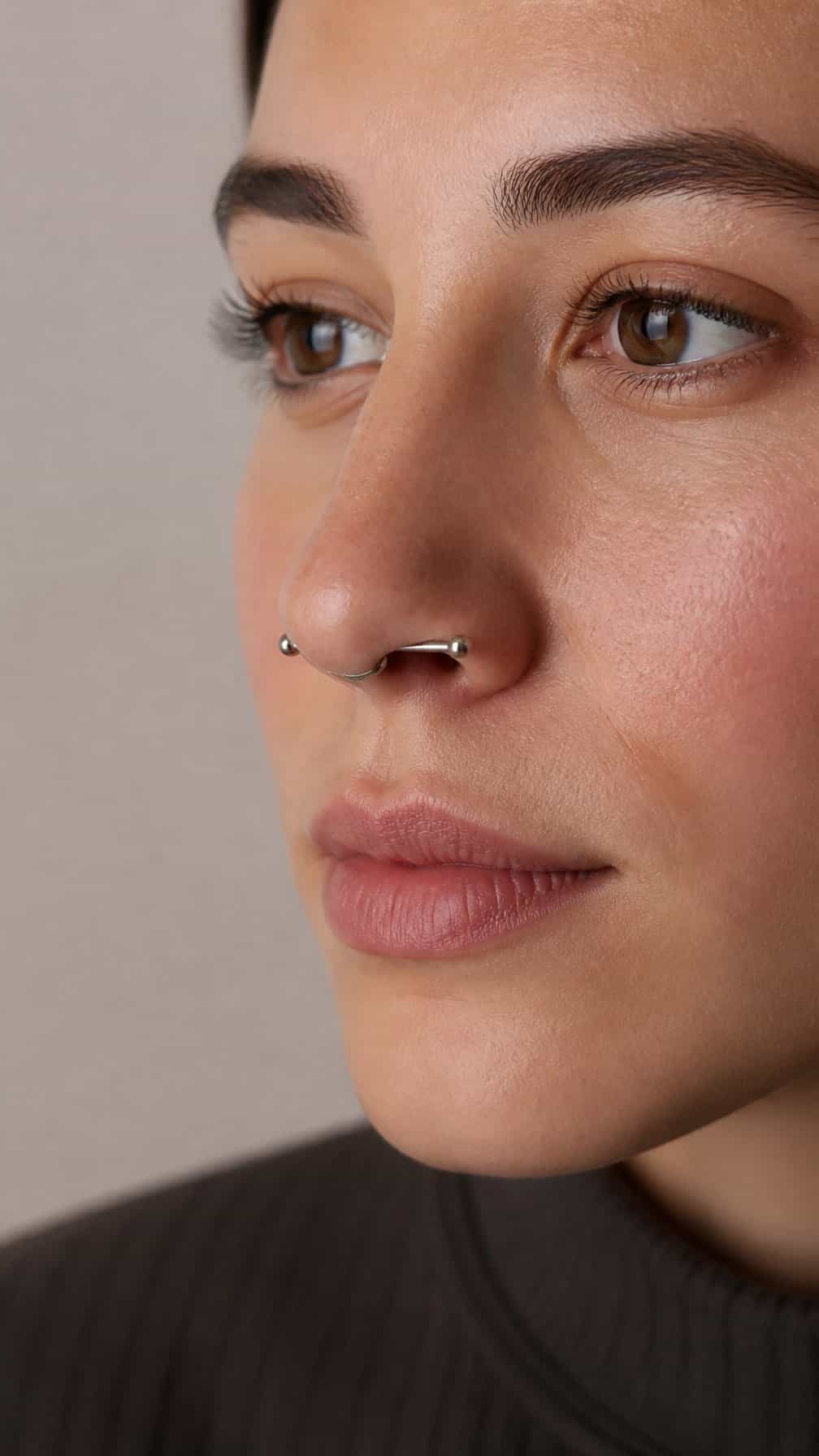 Close-up of a person wearing a straight barbell nasallang piercing through both nostrils and the nasal septum.