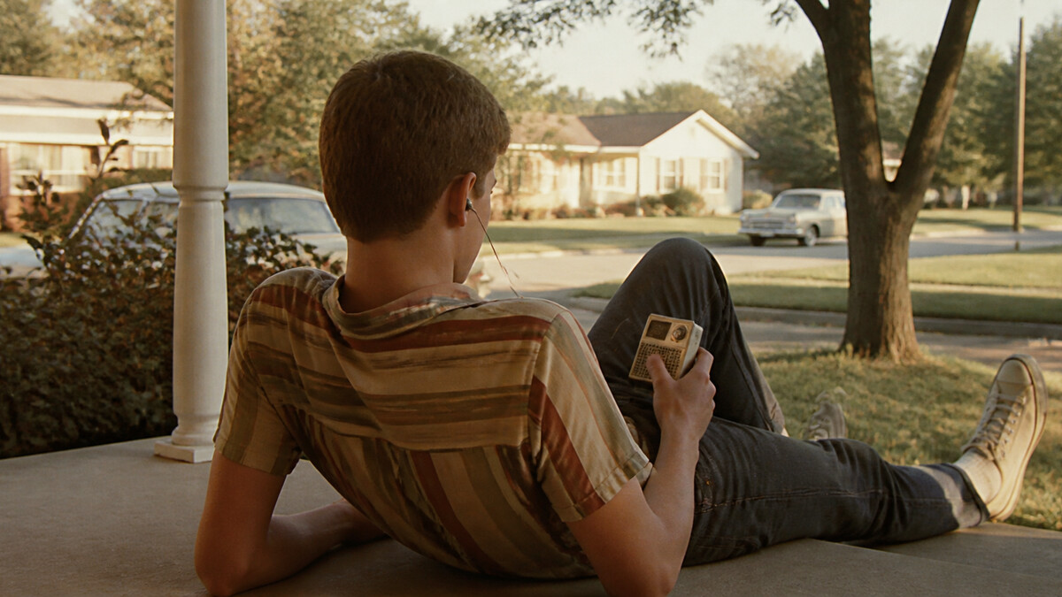 Teenager listening to a pocket transistor radio through one earpiece on a 1960s porch