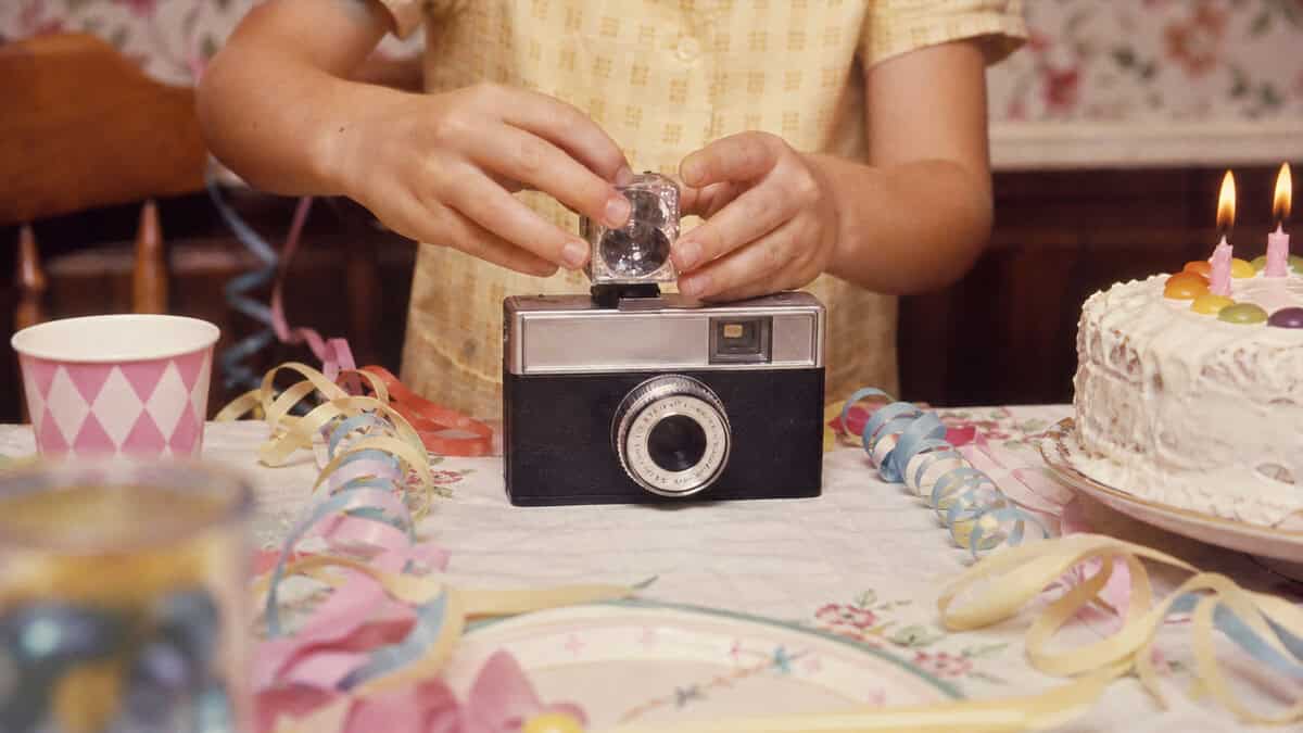 Child attaching a disposable flash cube to a compact camera at a 1960s birthday table