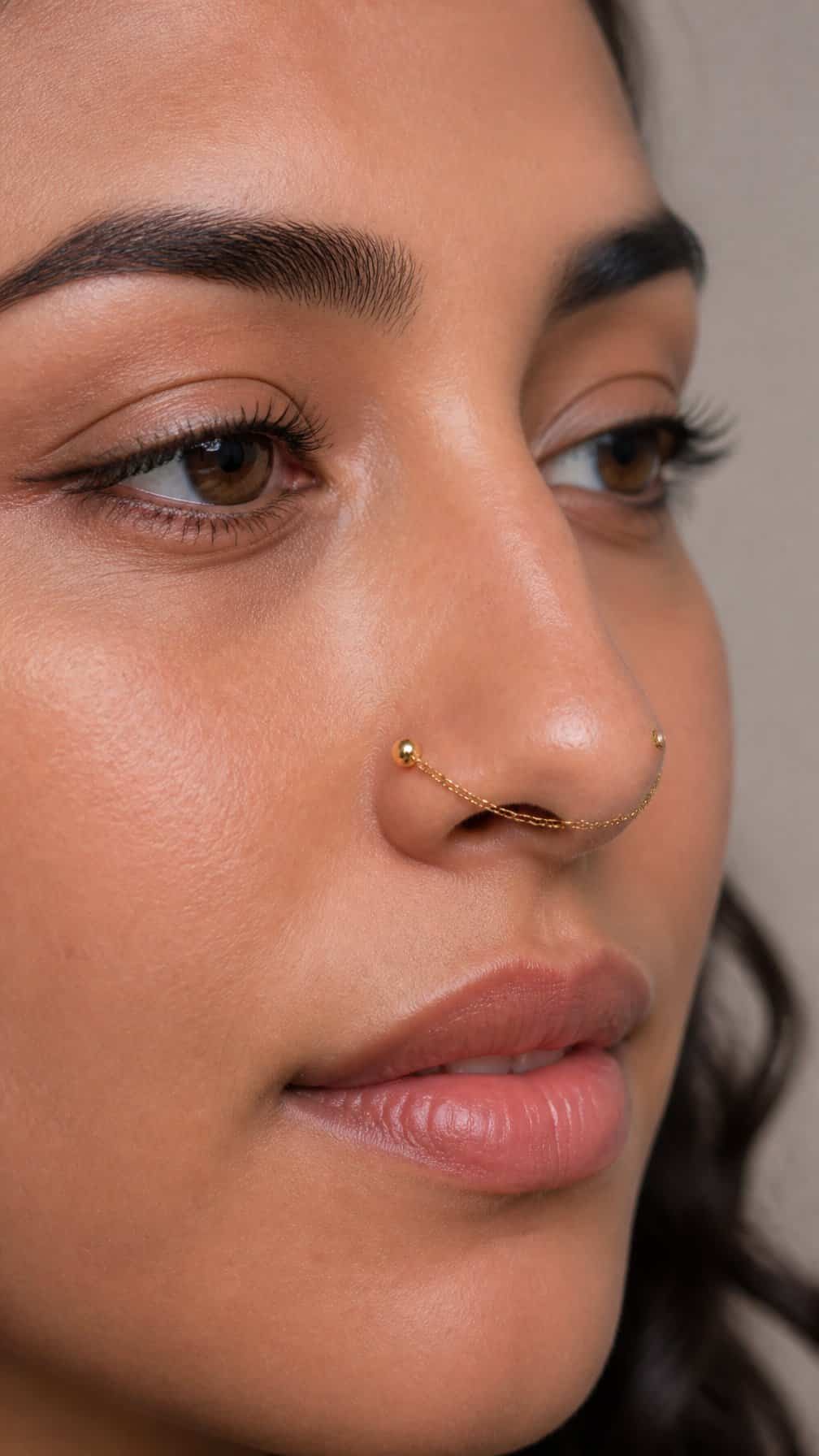 Close-up of a person wearing a delicate chain connecting two nostril piercings.