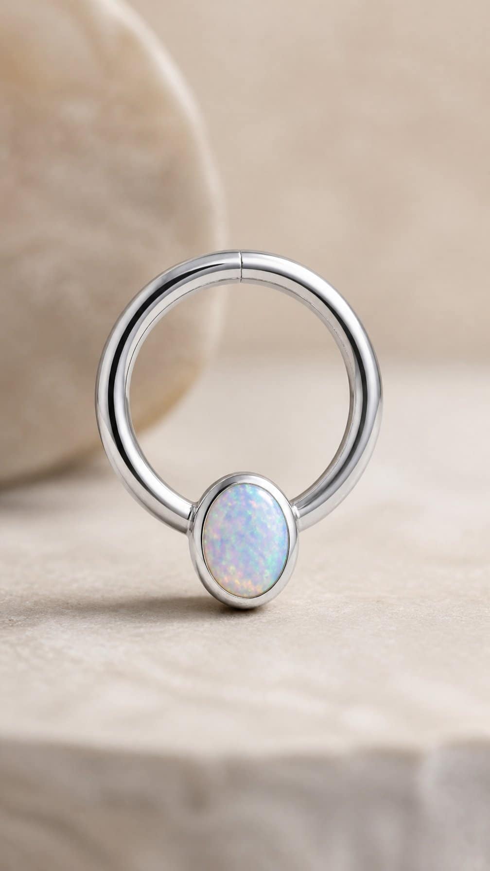 A polished seamless belly button ring with an iridescent opal accent resting on a neutral surface.