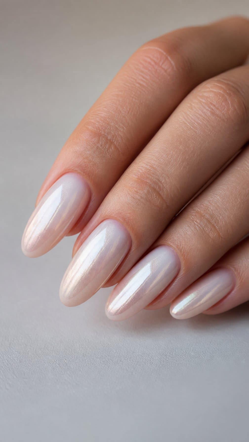 A hand displaying almond-shaped nails with a pearly white-to-chrome ombre manicure.