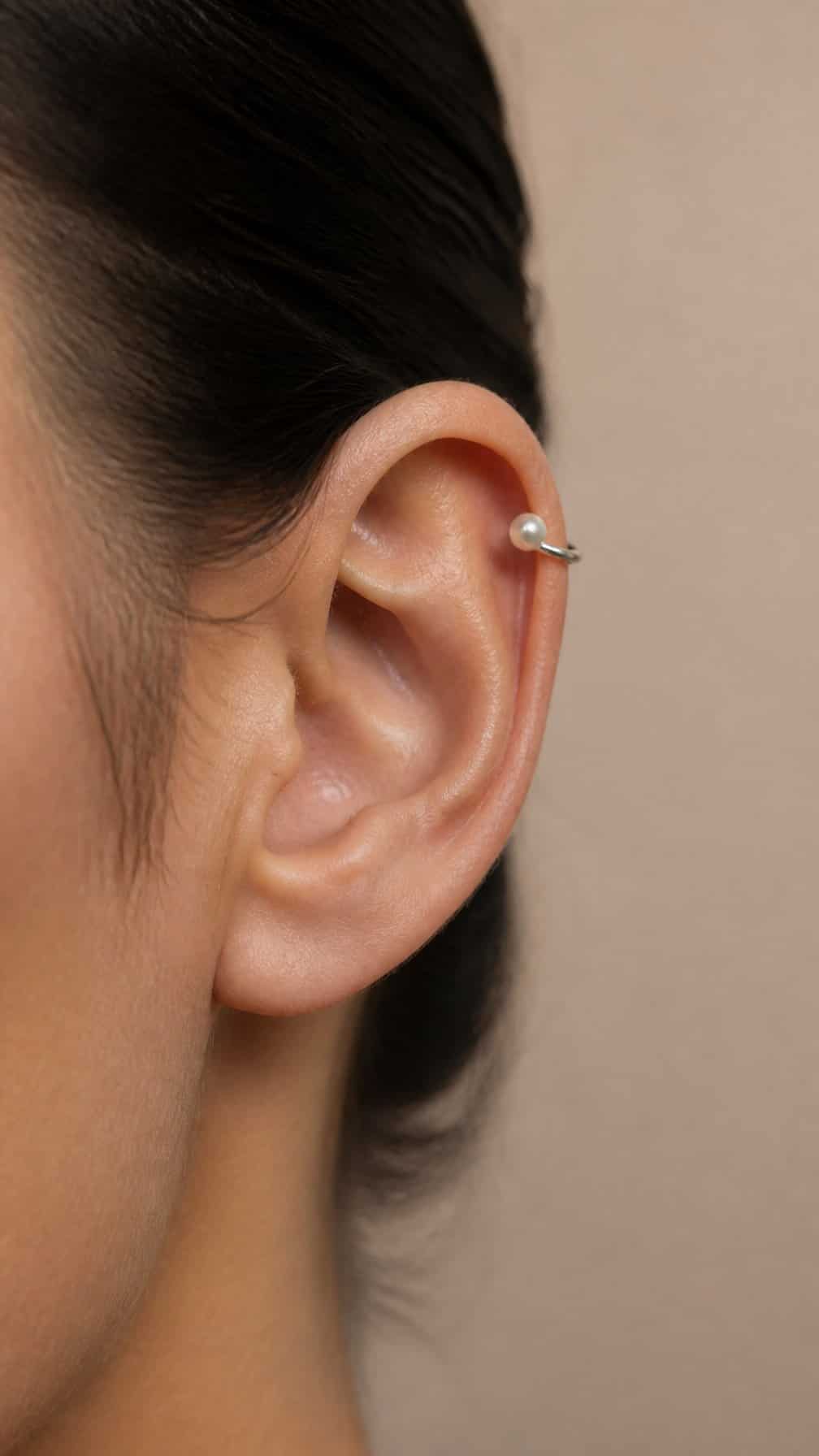 Close-up of an ear wearing a pearl-accented hoop piercing in the upper cartilage.