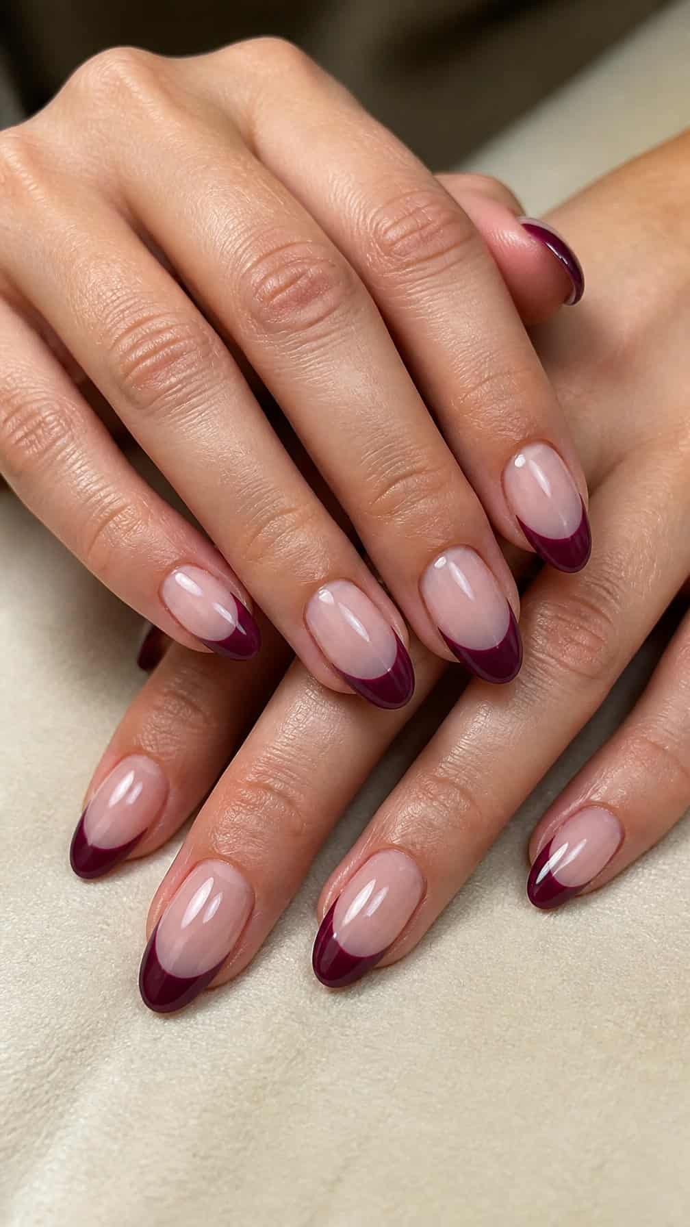 A hand with glossy plum French-tip nails resting on a neutral surface.