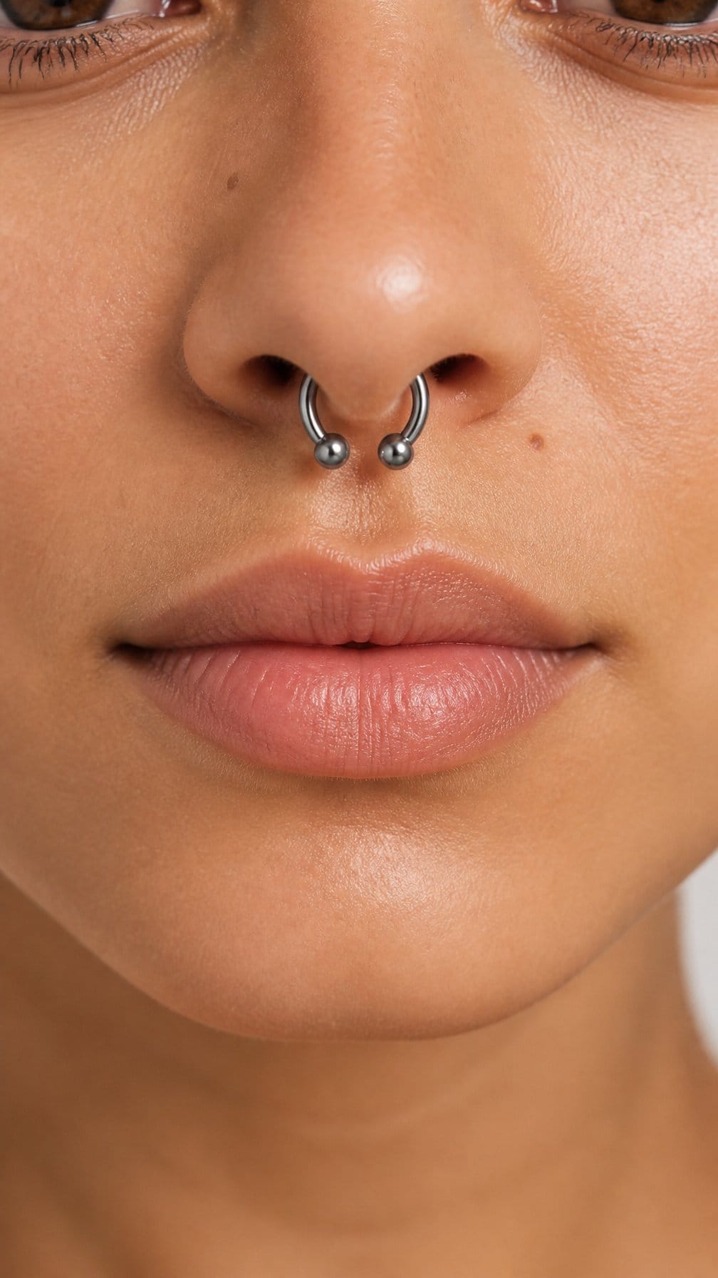 Close-up of a polished titanium circular barbell septum piercing on a person’s nose.