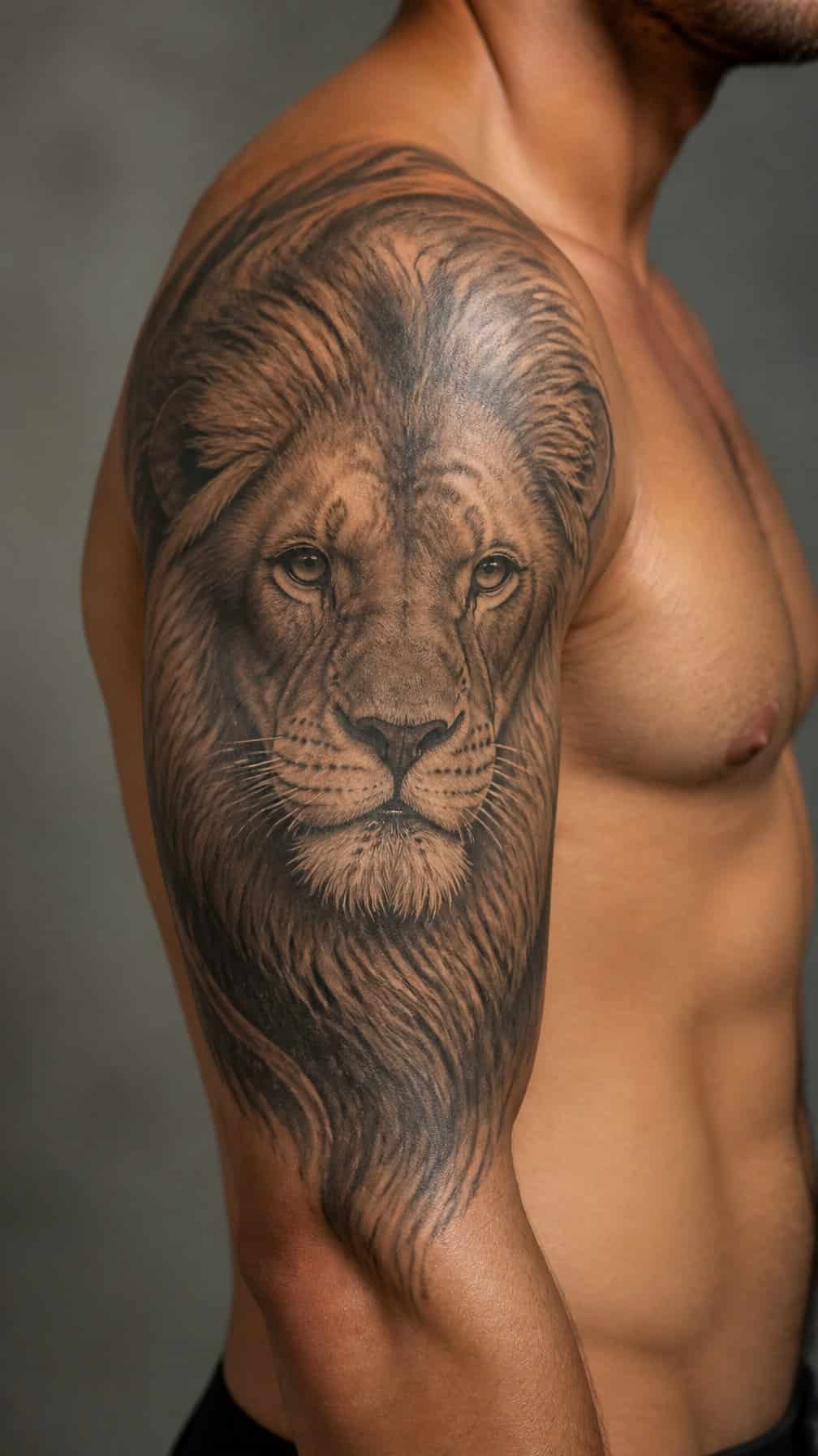 A realistic lion tattoo covers a person’s shoulder and extends onto the upper arm.