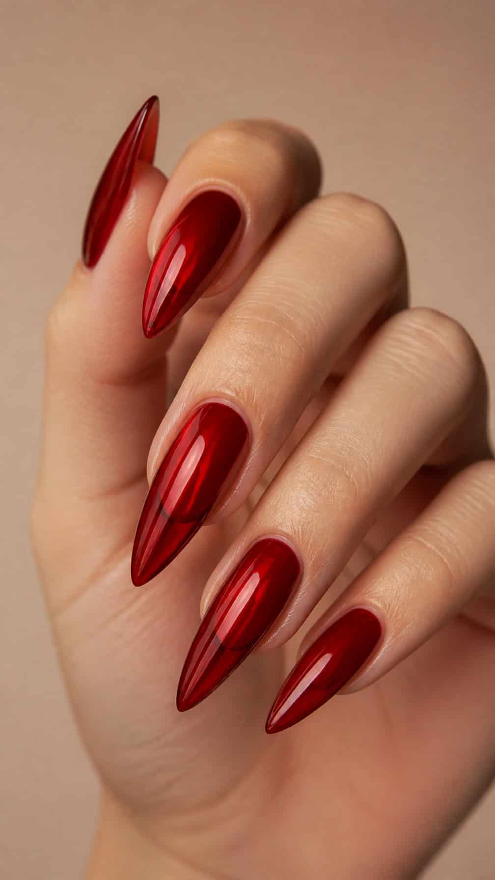 A hand with long, pointed glossy red nails posed against a neutral background.