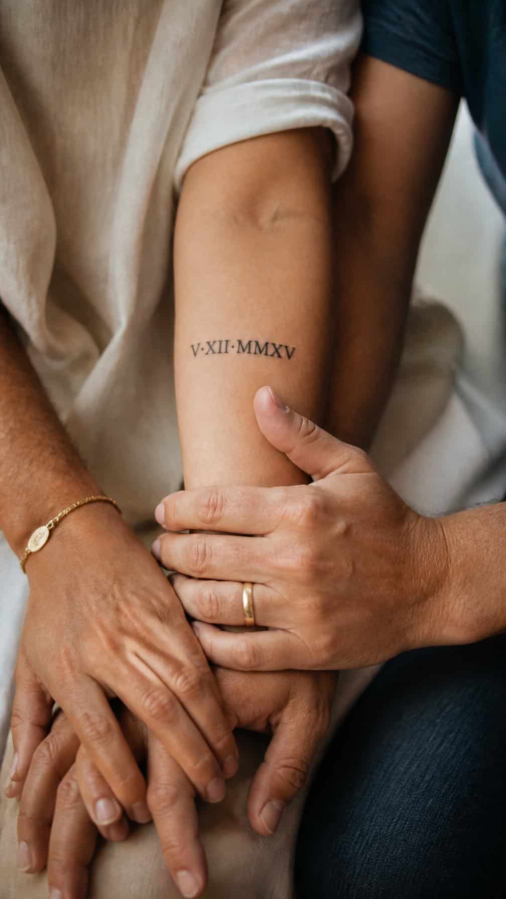 Family members gently place their hands together, with a small Roman numeral date tattoo visible on one forearm.