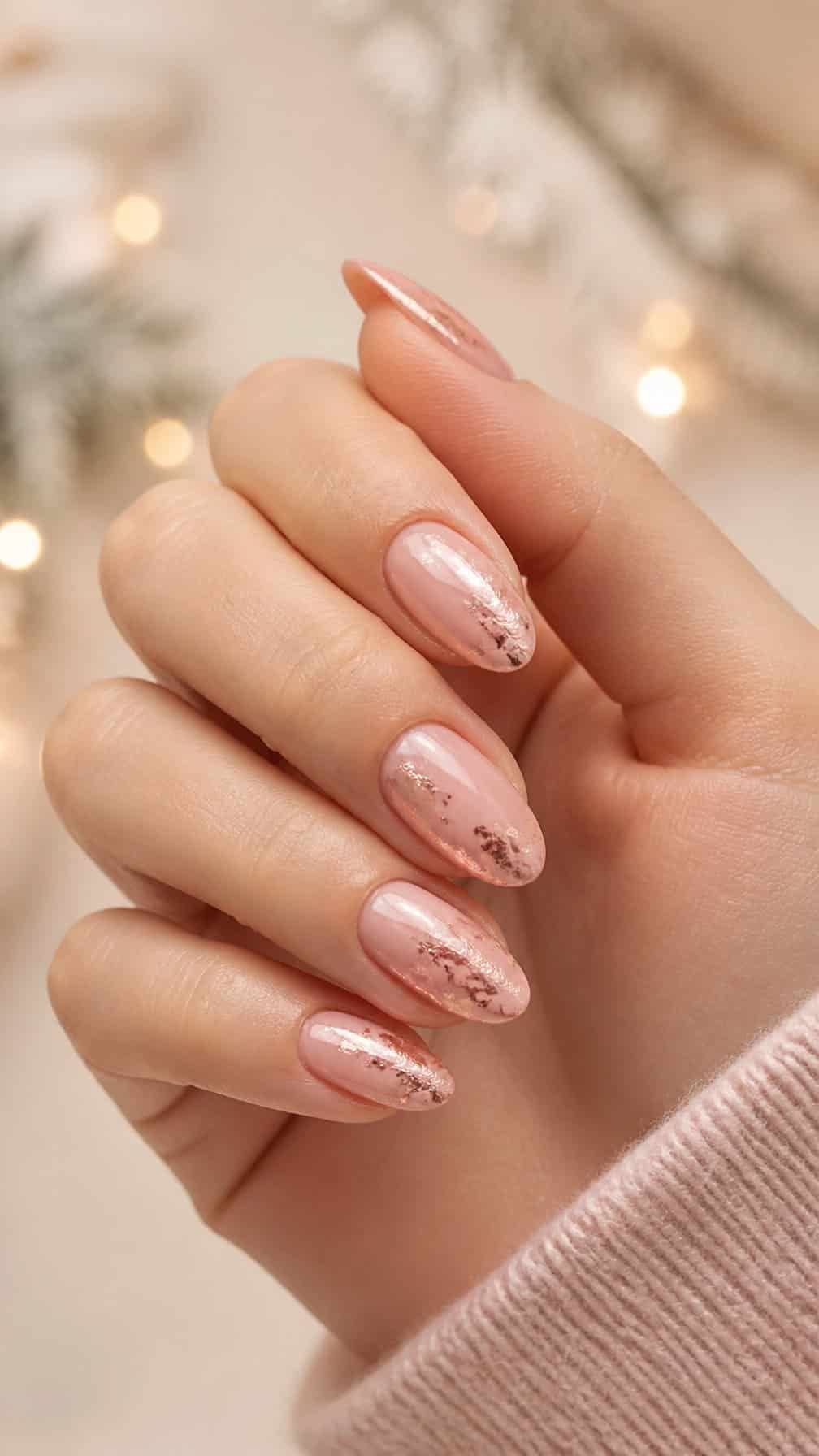 A hand with soft pink almond-shaped nails decorated with rose gold foil accents.