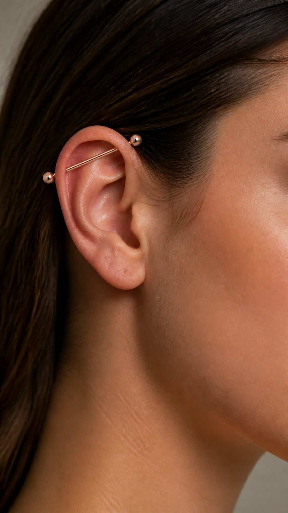 Close-up of an ear wearing a polished rose gold industrial barbell piercing.