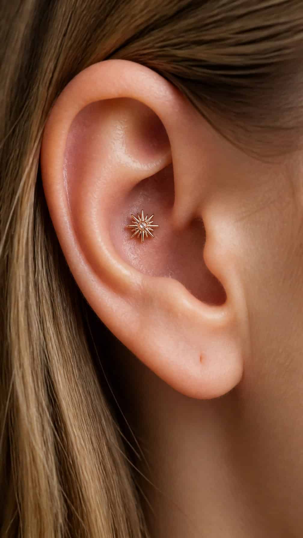 Close-up of an ear wearing a rose gold starburst stud in a conch piercing.