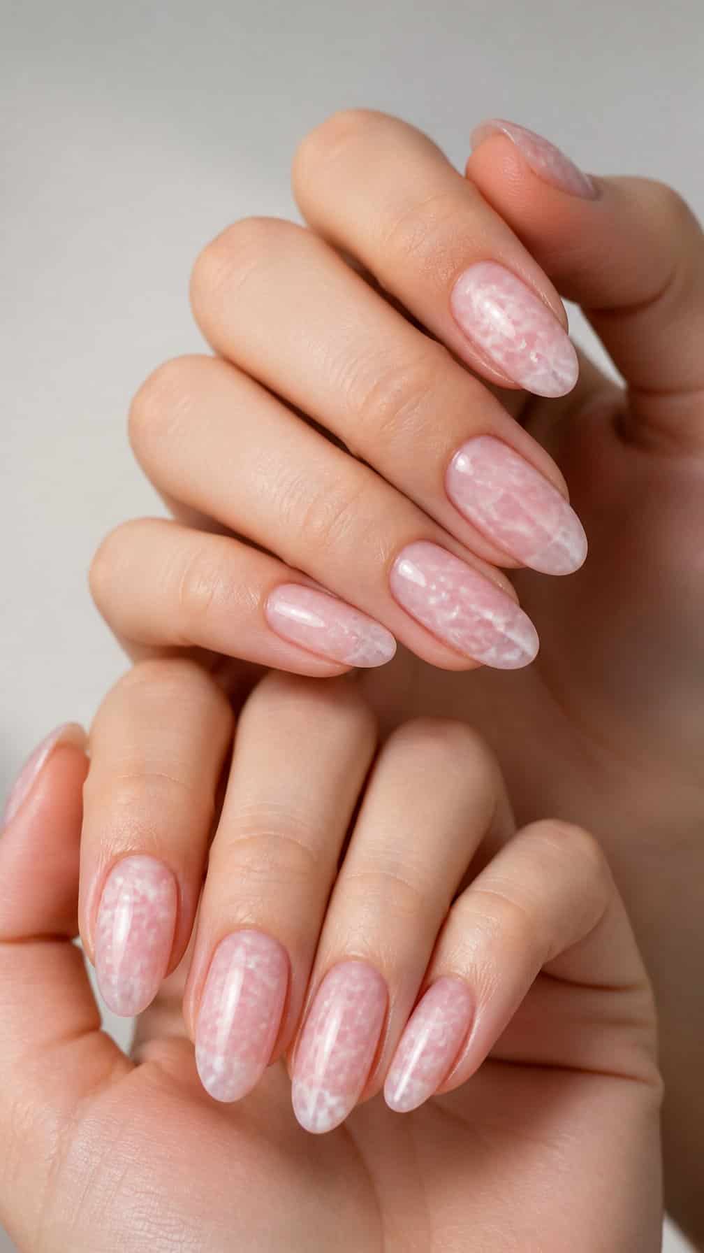 Close-up of hands with glossy pink and white marble-patterned almond-shaped nails.