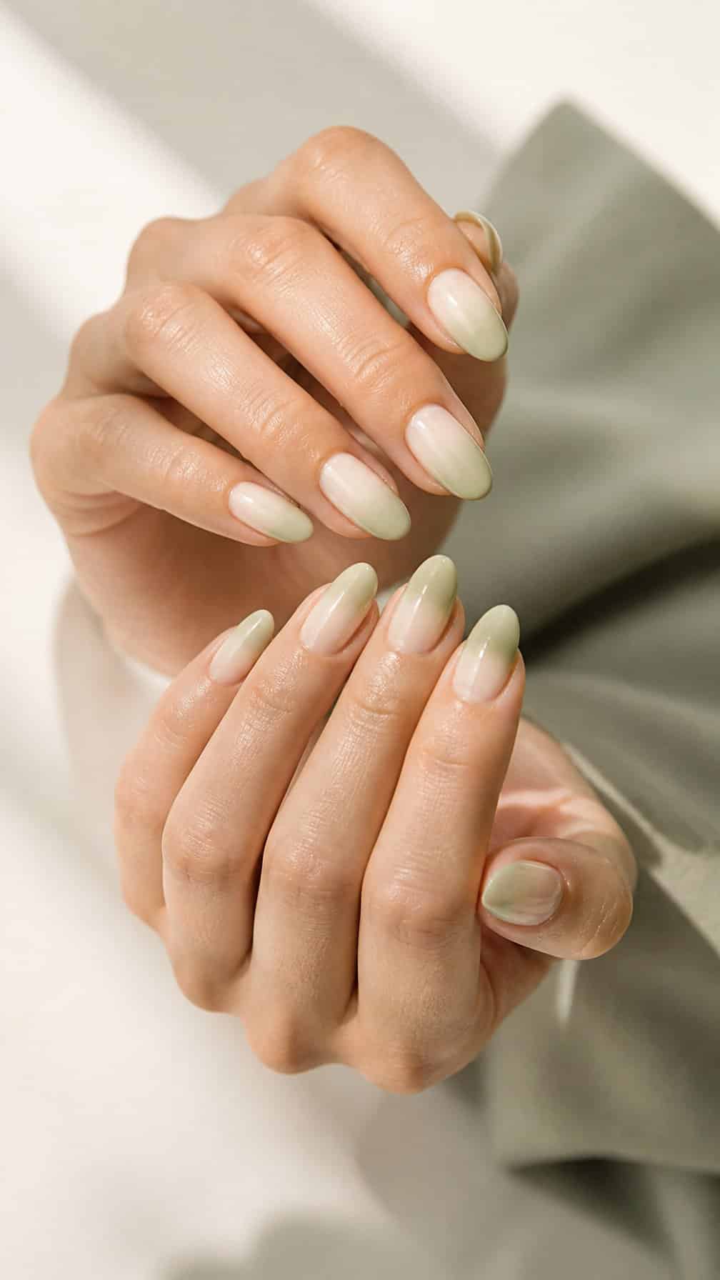 Close-up of a hand with almond-shaped nails featuring a sage green to ivory gradient.