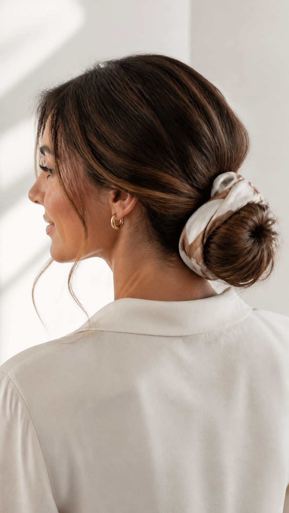 Woman with long hair styled in a low bun wrapped with a scarf.