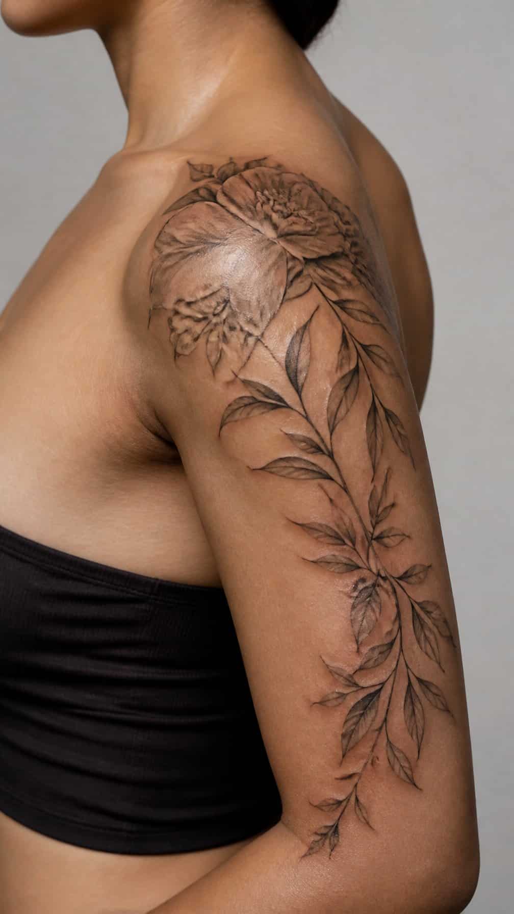 A person displays a botanical tattoo curving from the shoulder down the upper arm.