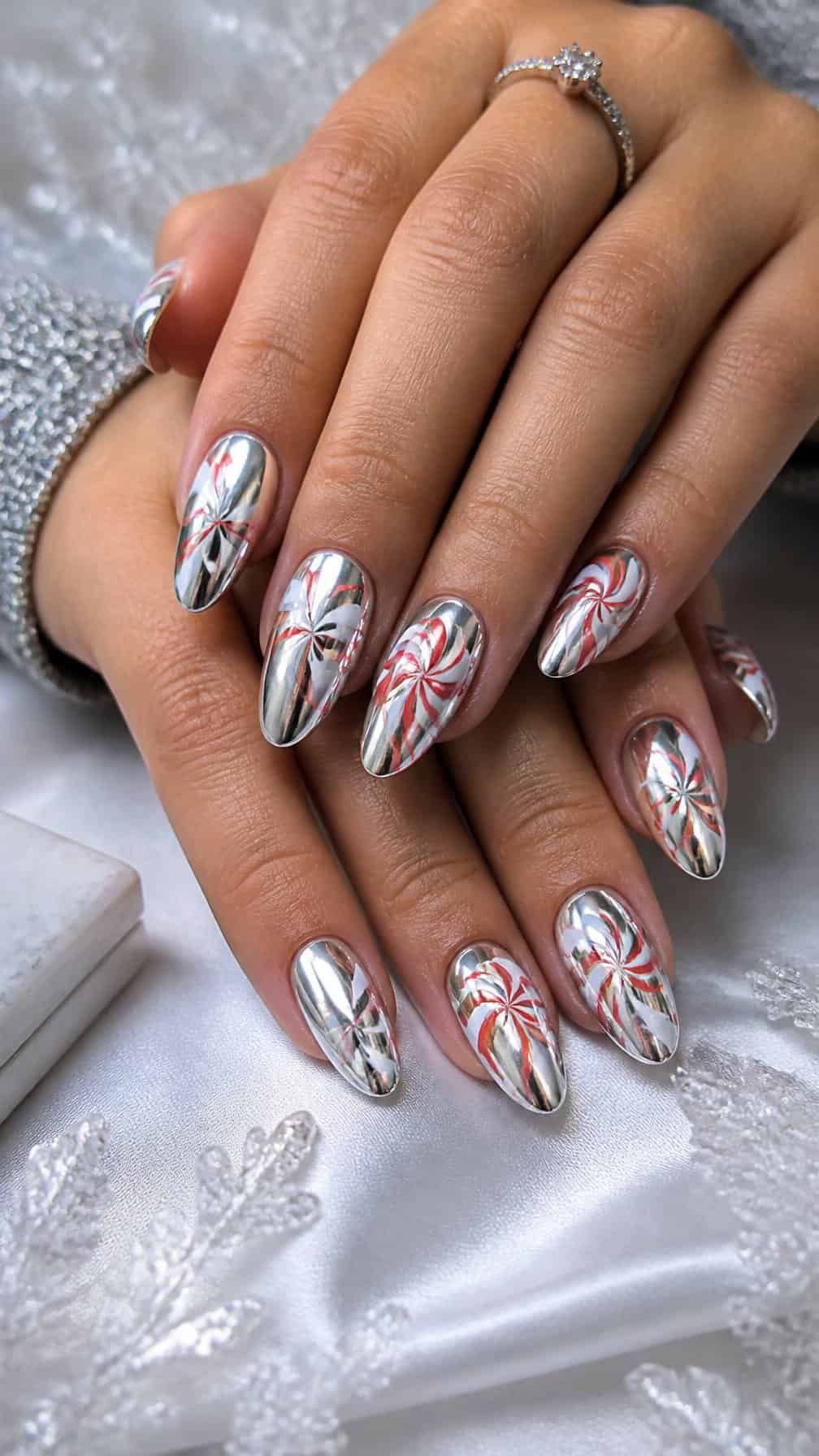 Close-up of a hand with silver chrome nails featuring white and candy-red peppermint swirls.