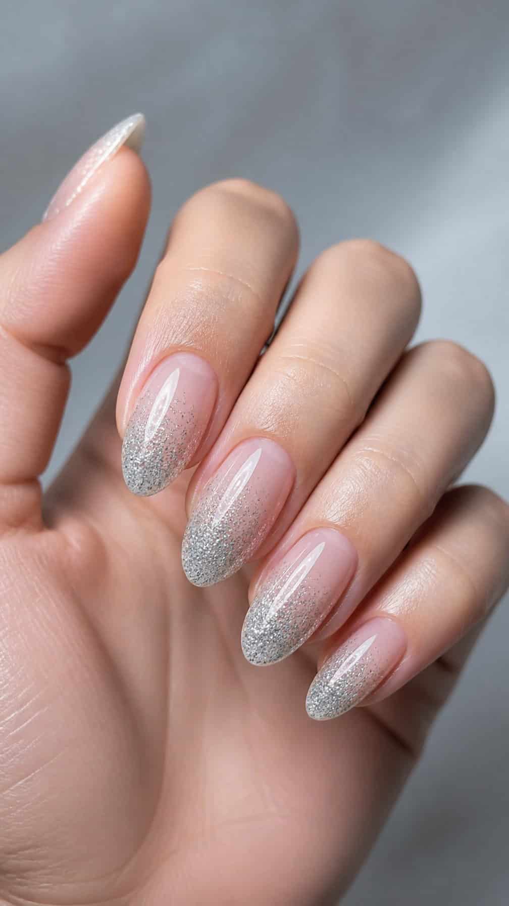 A hand displaying almond-shaped nails with a silver glitter ombre manicure.