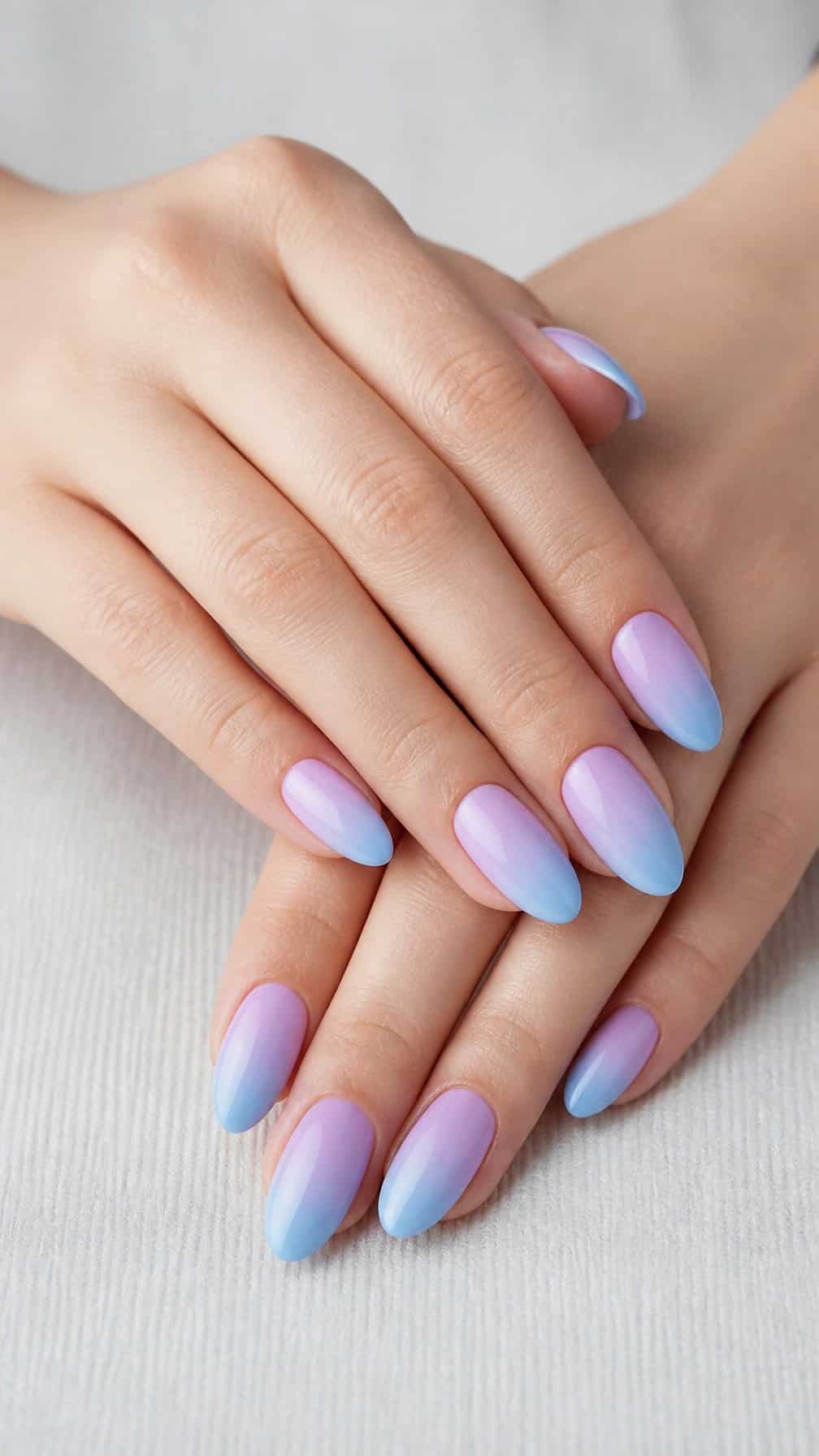 A hand displaying almond-shaped nails with a sky-blue and lilac gradient manicure.
