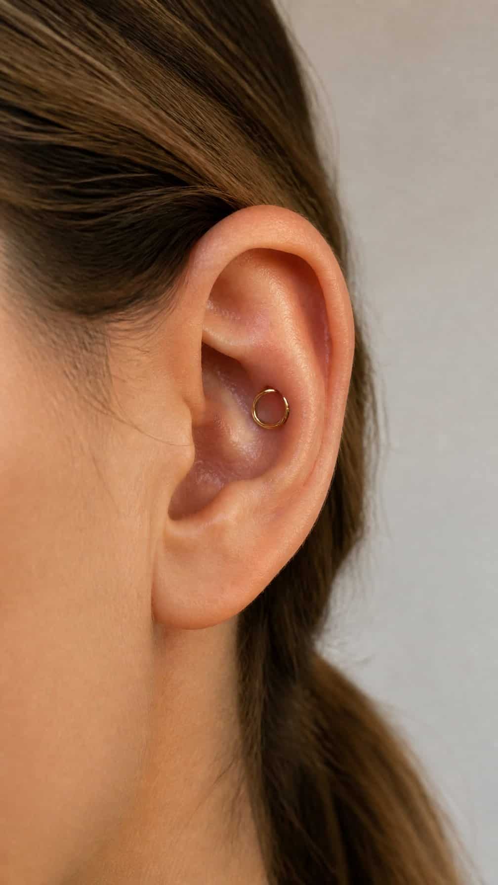 Close-up of an ear wearing a small seamless hoop in the conch piercing.