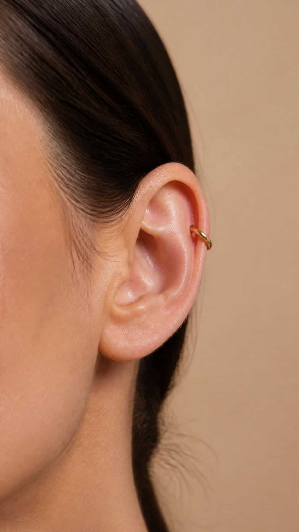 Close-up of an ear wearing a small gold huggie ring in a helix piercing.