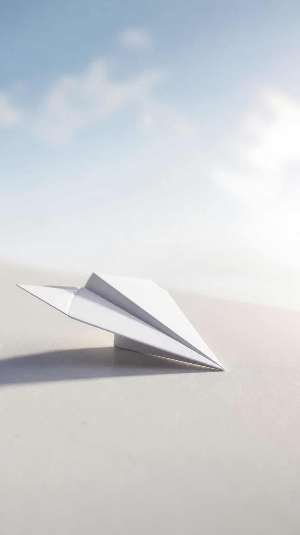 A small white paper airplane rests on a pale surface in soft natural light.