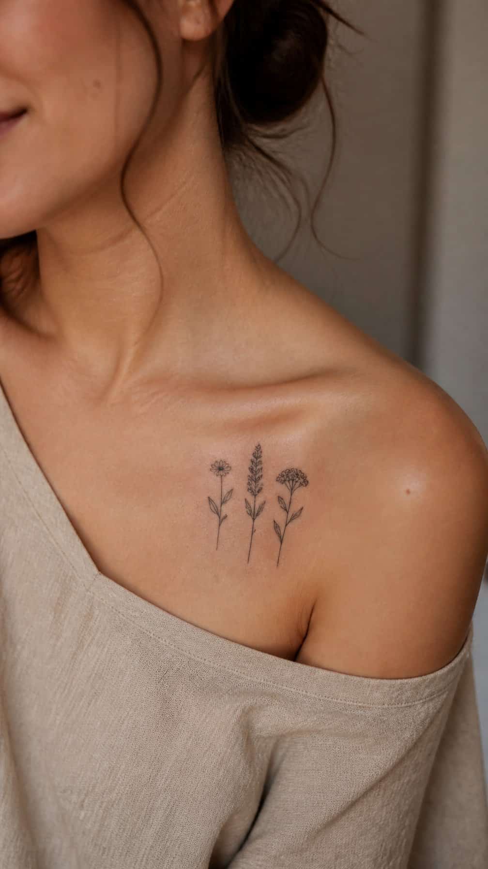 A small trio of wildflower tattoo stems rests near the shoulder end of a visible collarbone.