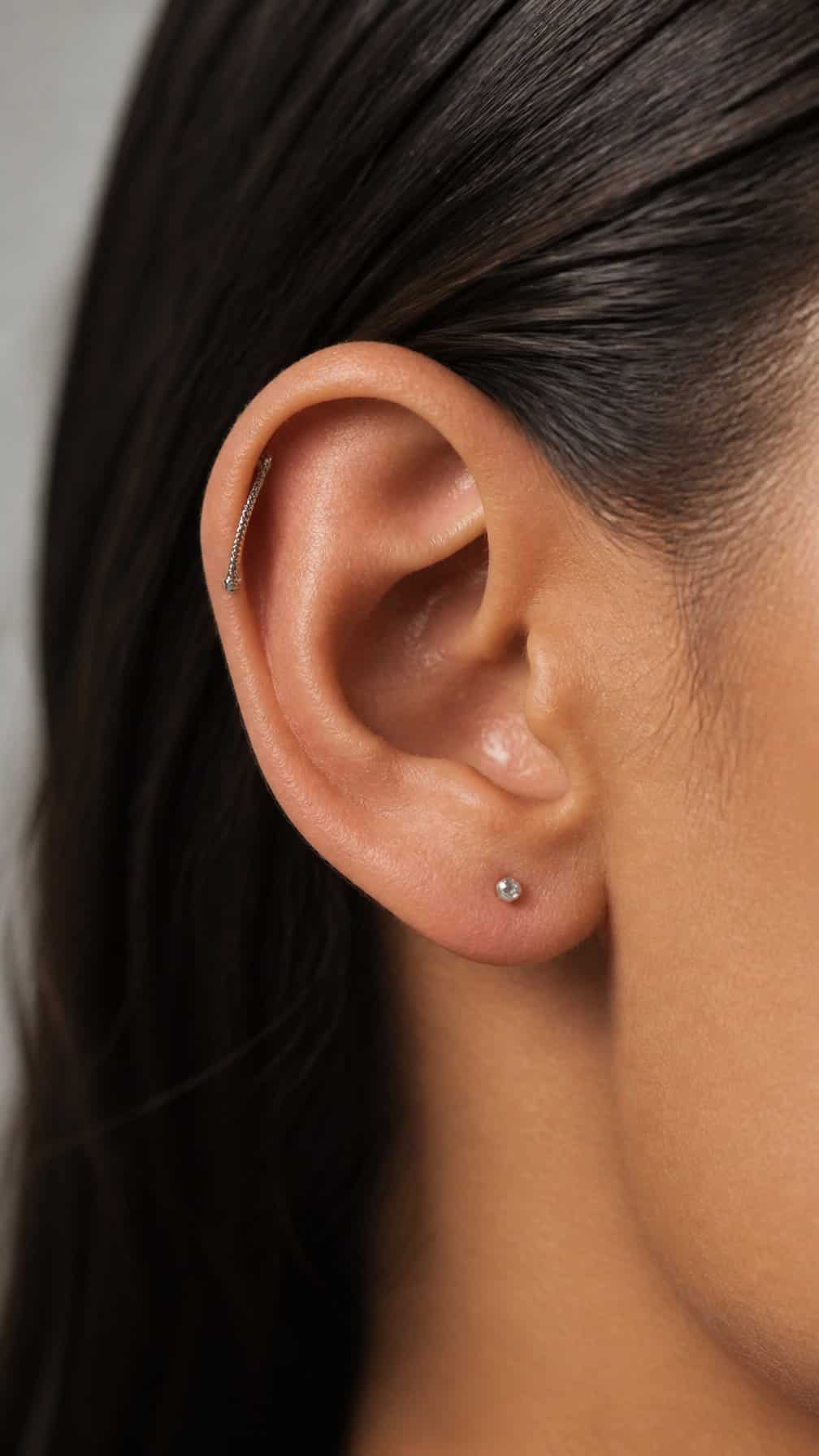 Close-up of an ear with a delicate snake-chain piercing curving along the upper cartilage.