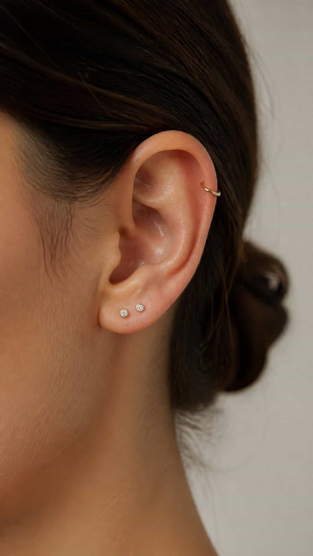 Close-up of an ear with two lobe piercings and one helix piercing.