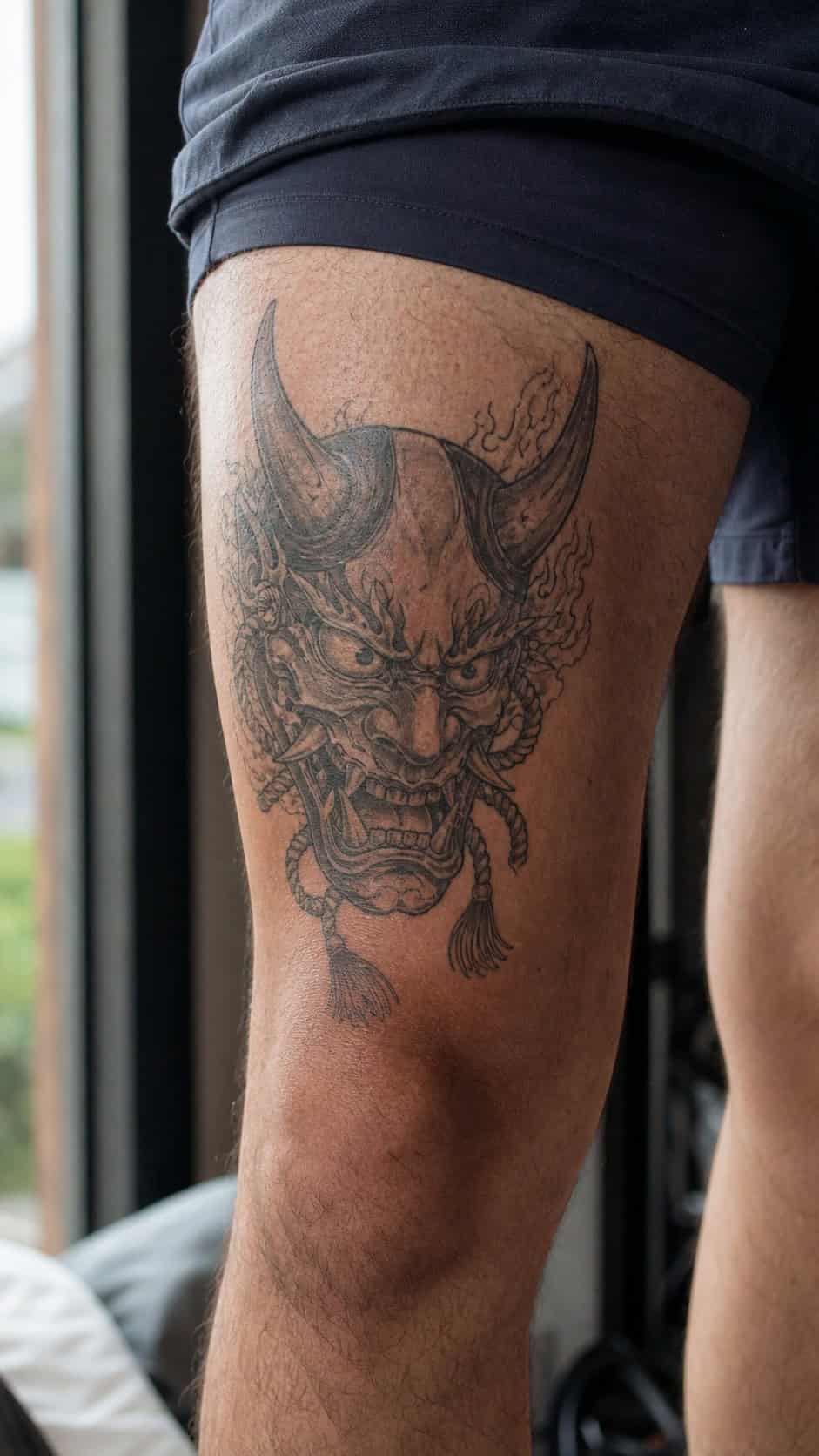 From Samurai to Dragons: 19 Stunning Japanese Tattoo Ideas for Men 13 Healed oni mask tattoo on a adult man's outer thigh, photographed in a natural relaxed documentary crop — study 2