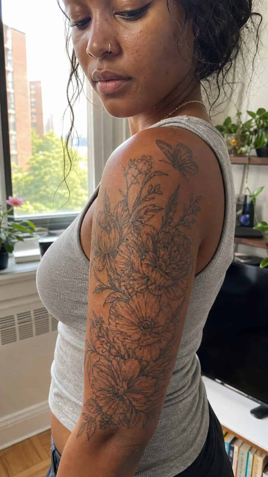 Healed floral half-sleeve tattoo on a adult woman's upper-arm sleeve, photographed in a natural gentle side angle that clearly shows — study 1