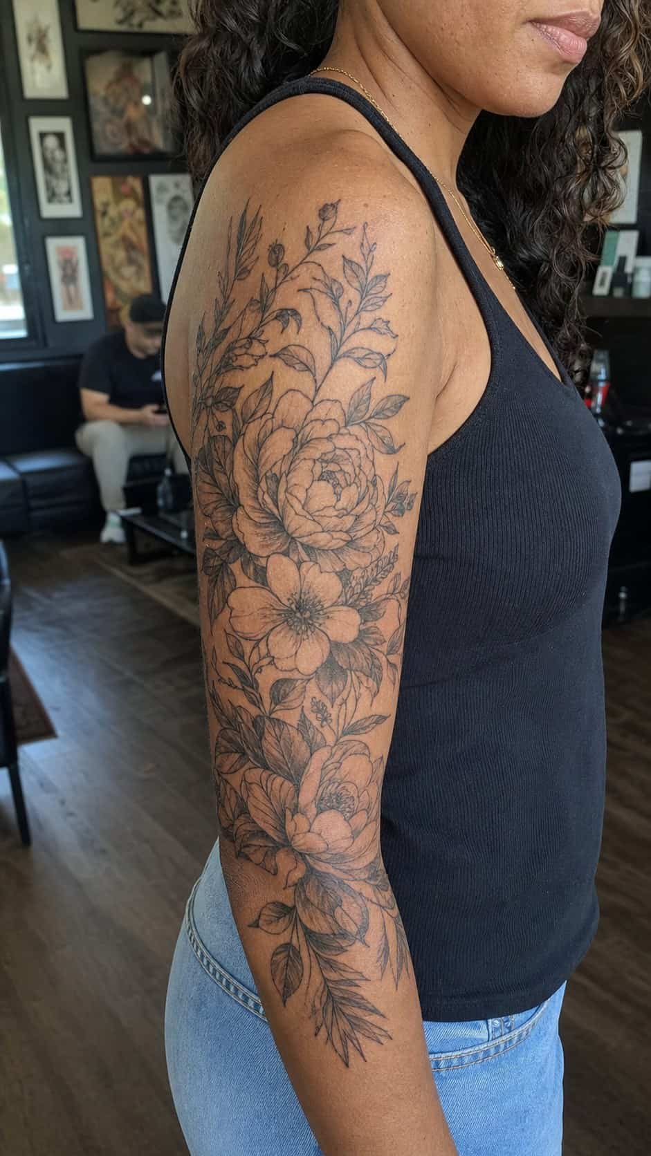 Healed floral half-sleeve tattoo on a adult woman's upper-arm sleeve, photographed in a natural slightly elevated close view — study 2