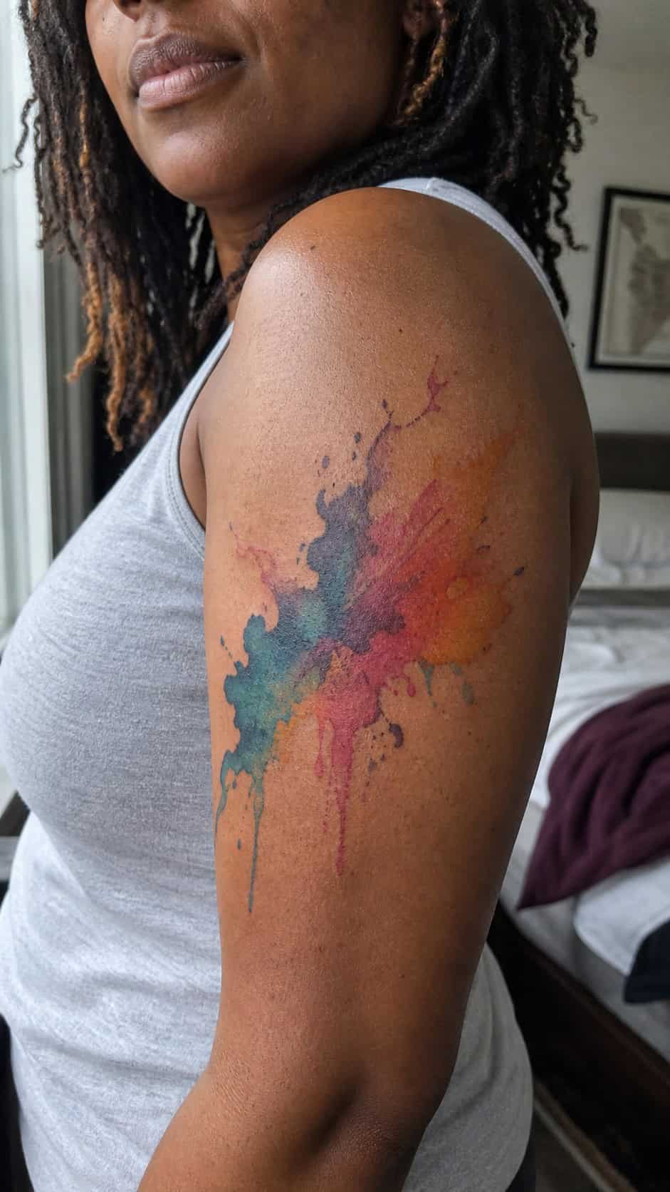 Healed artistic watercolor splash tattoo on a adult woman's outer upper arm, photographed in a natural casual close three-quarter view — study 1