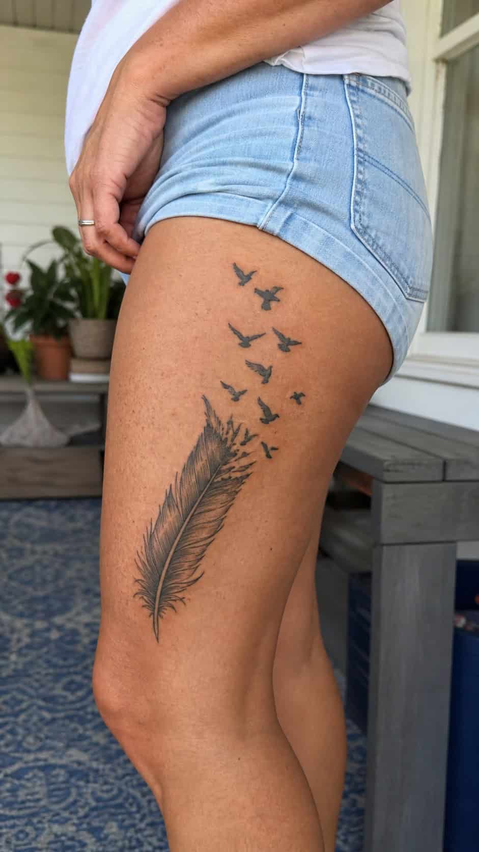Healed feather and birds tattoo on a adult woman's outer thigh, photographed in a natural relaxed documentary crop — study 1
