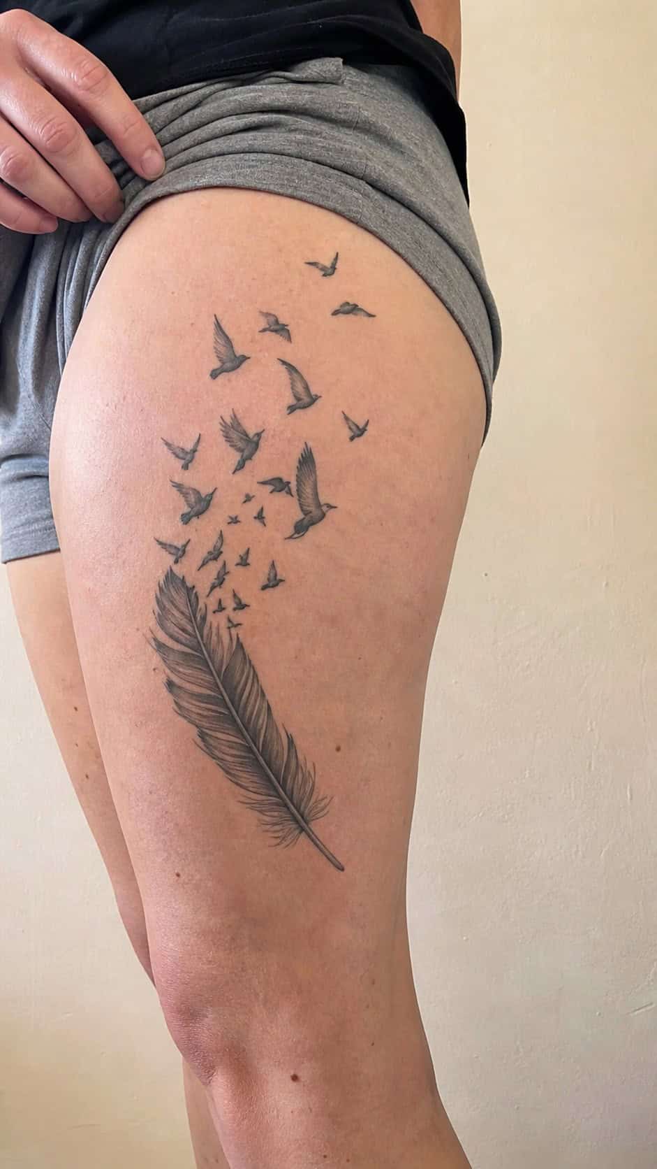 Healed feather and birds tattoo on a adult woman's outer thigh, photographed in a natural casual close three-quarter view — study 2