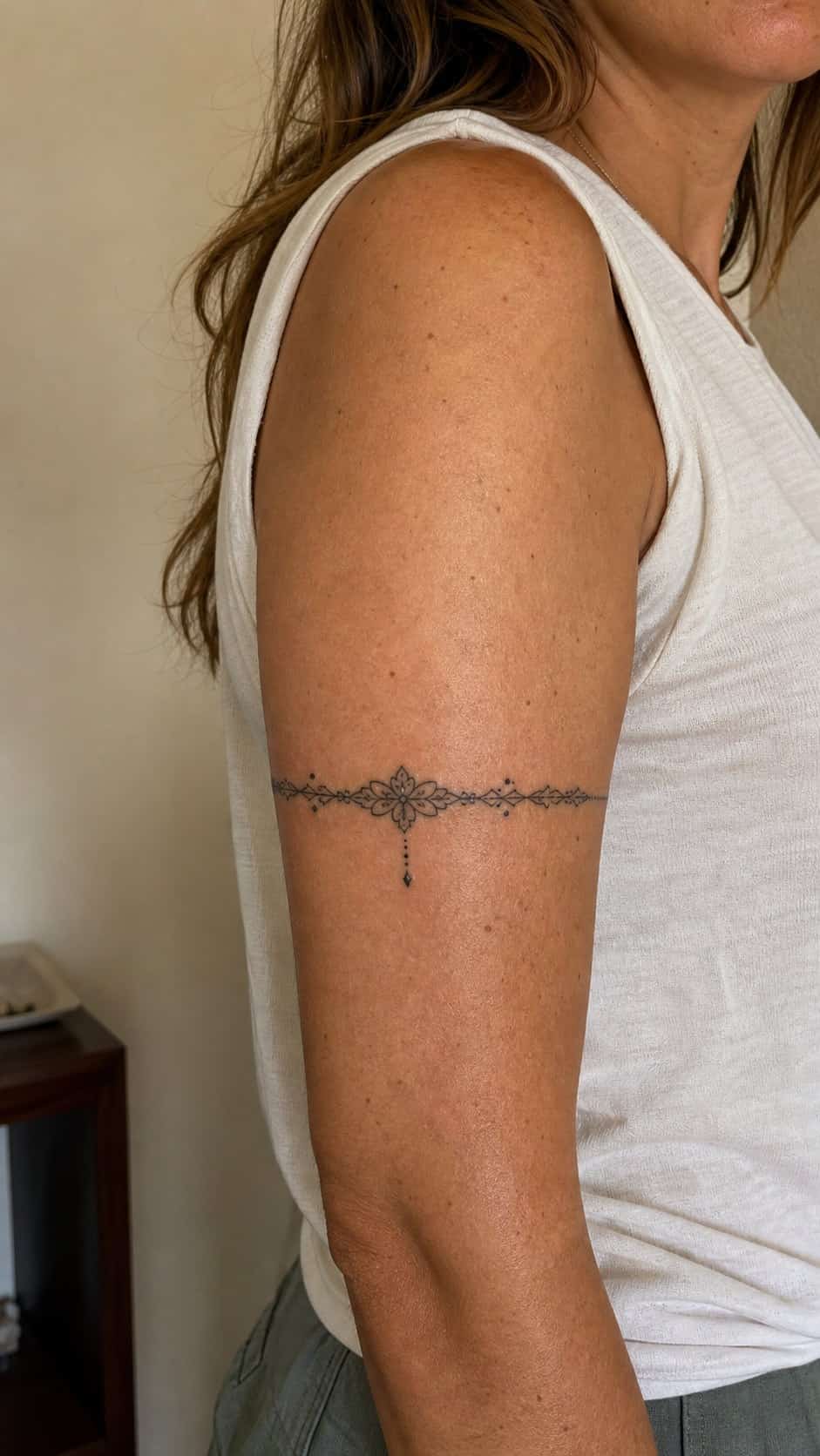 Healed chic bracelet design tattoo on a adult woman's outer upper arm, photographed in a natural straight-on close view, a touch — study 1