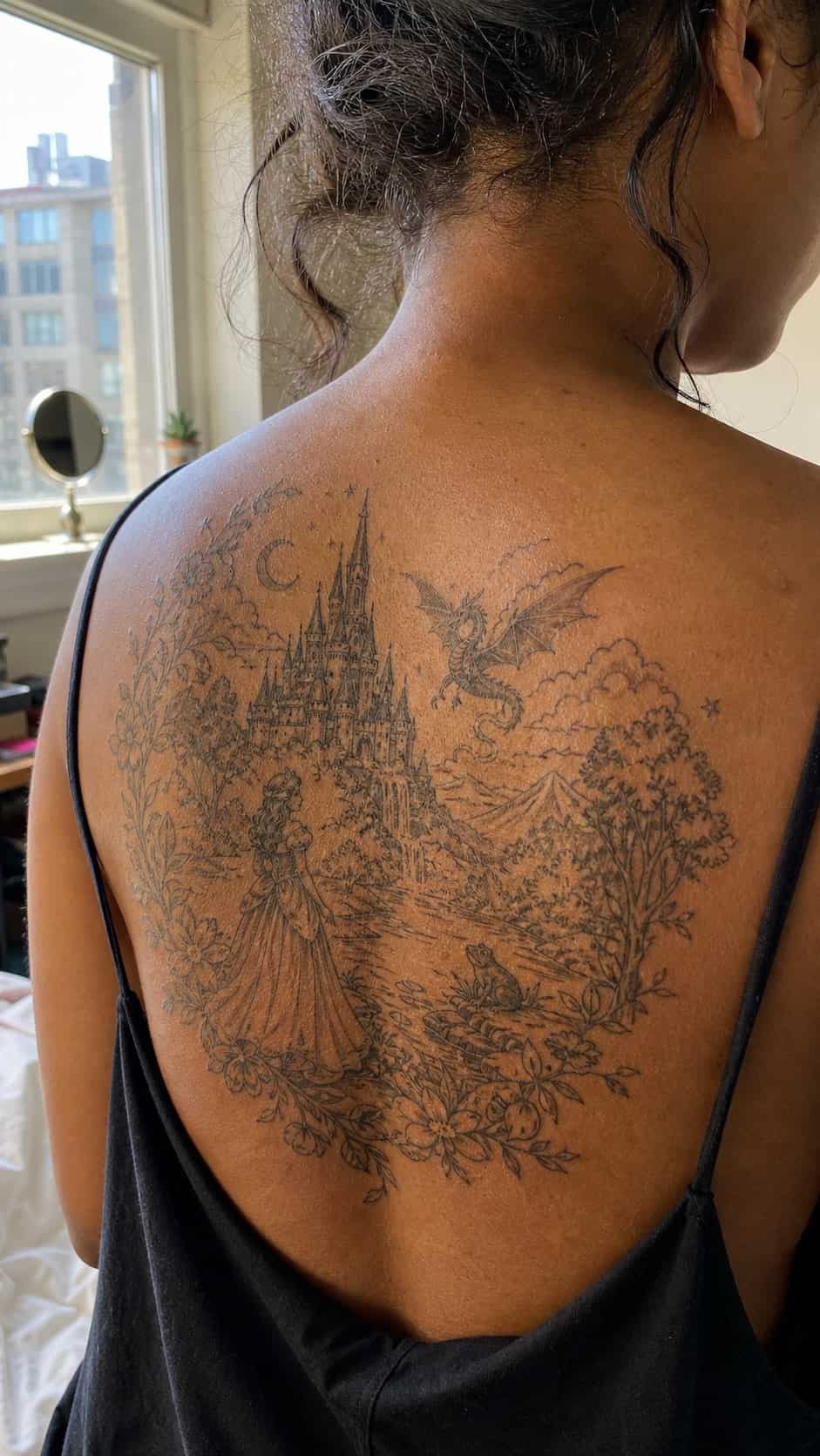 Healed enchanting fairy tale scene tattoo on a adult woman's upper back, photographed in a natural straight-on close view, a touch — study 2