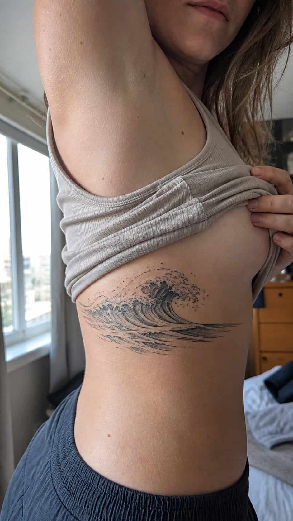 32 Stunning Rib Tattoos for Women 17 Healed ocean waves tattoo on a adult woman's side ribs, photographed in a natural casual close three-quarter view — study 2
