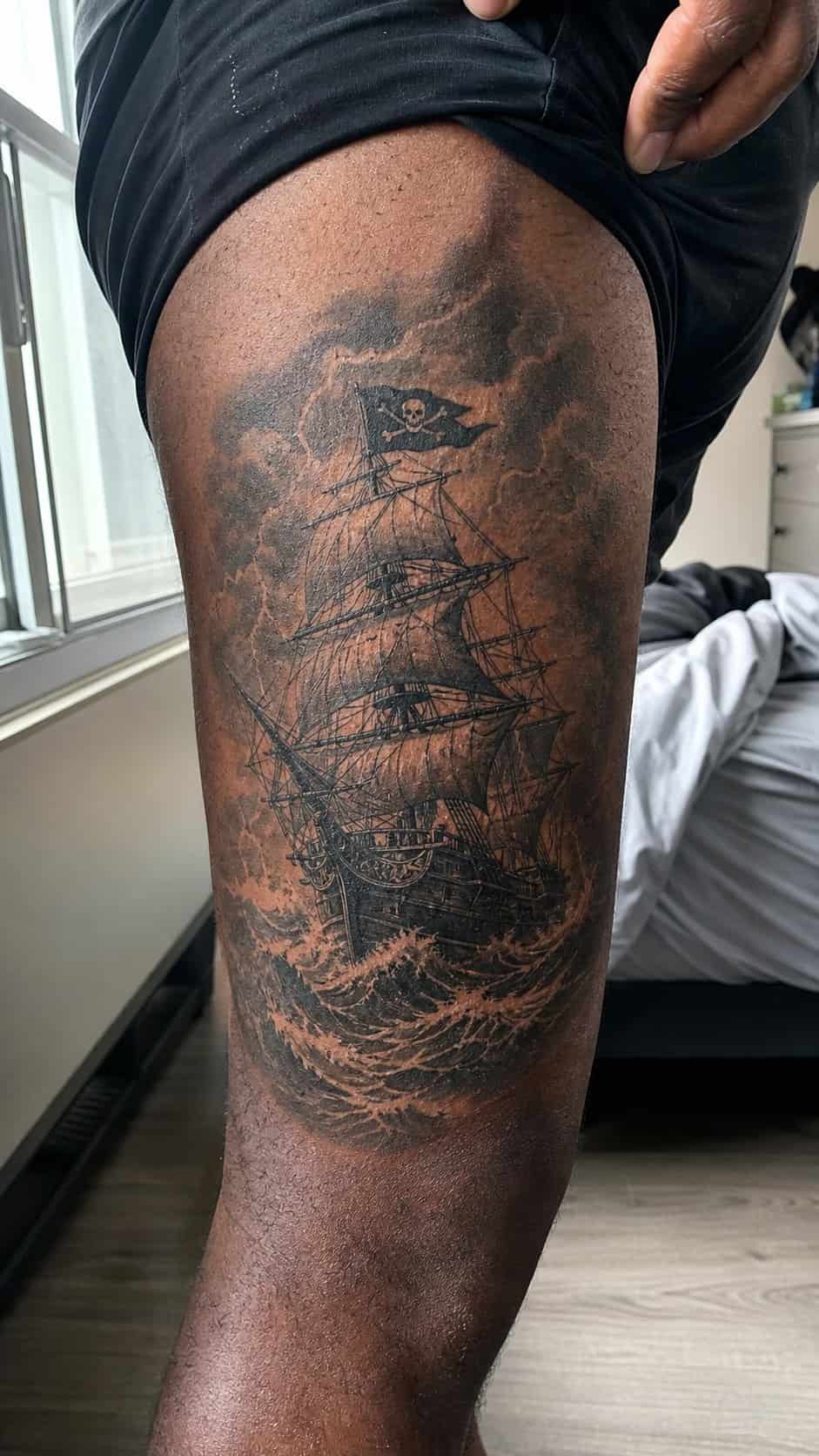 Feeling Bold? Try These 25 Killer Thigh Tattoo Ideas for Men 33 Healed pirate ship in stormy seas tattoo on a adult man's outer thigh, photographed in a natural relaxed documentary crop — study 1