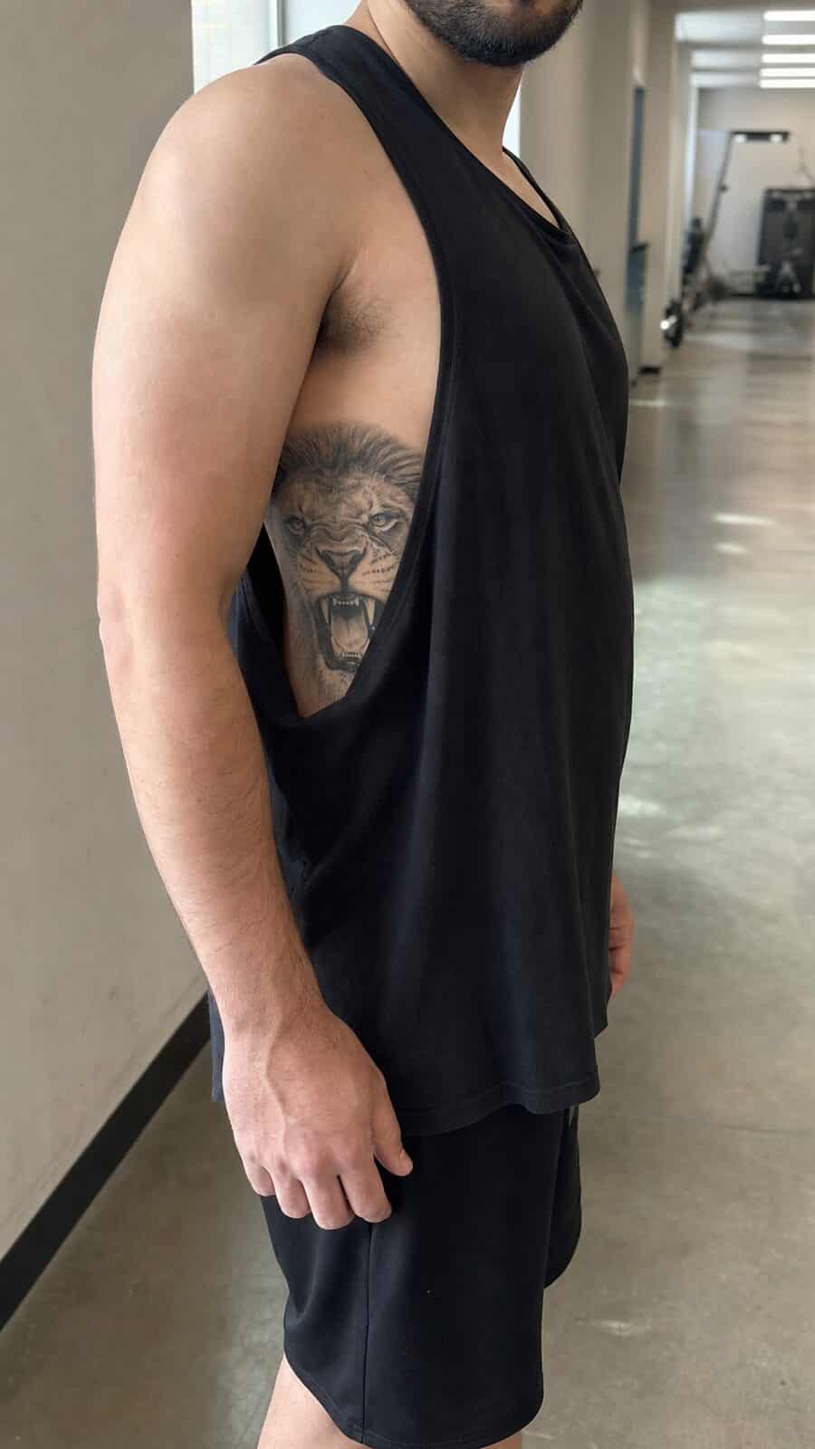 Healed fierce lion tattoo on a adult man's side ribs, photographed in a natural casual close three-quarter view — study 1