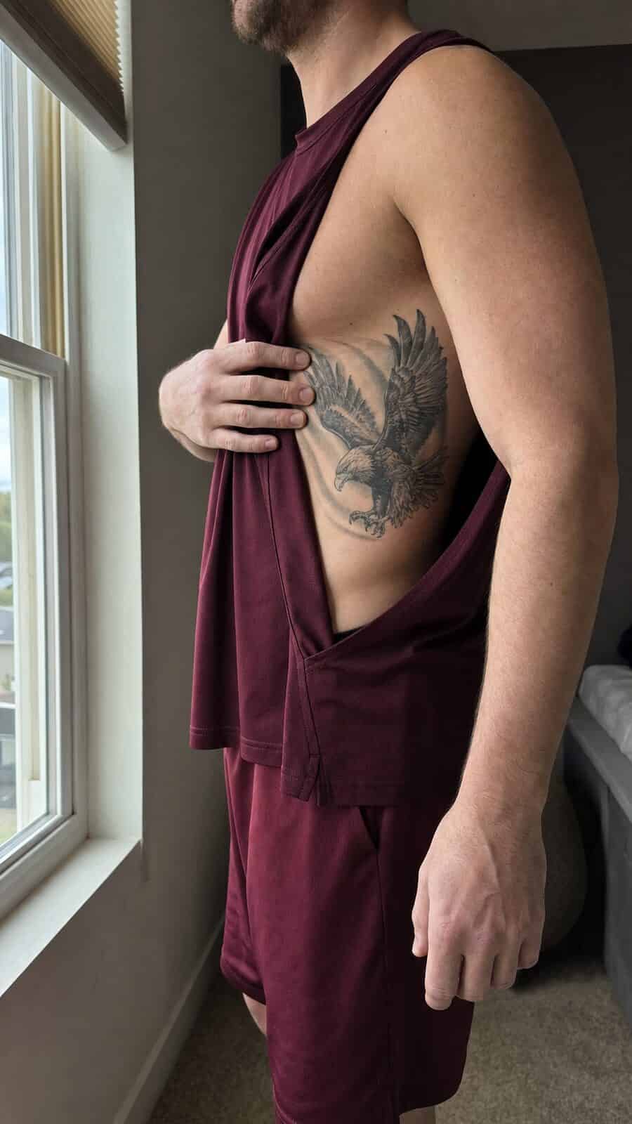Healed majestic eagle tattoo on a adult man's side ribs, photographed in a natural casual close three-quarter view — study 2