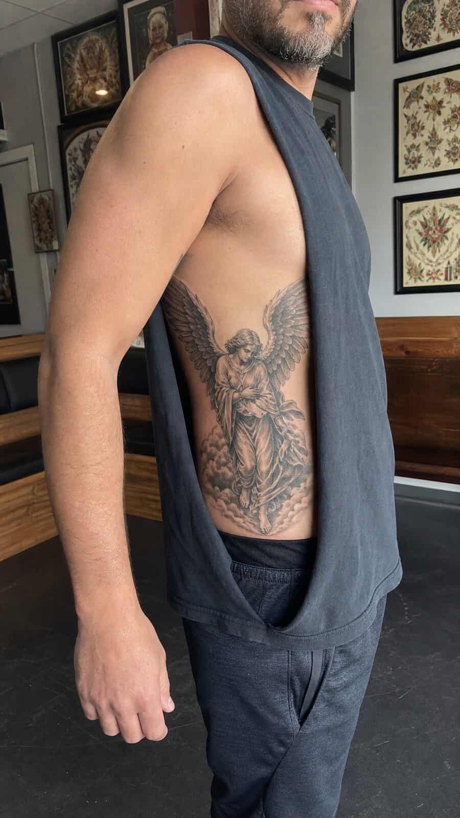 Healed guardian angel tattoo on a adult man's side ribs, photographed in a natural gentle side angle that clearly shows how the ink — study 1
