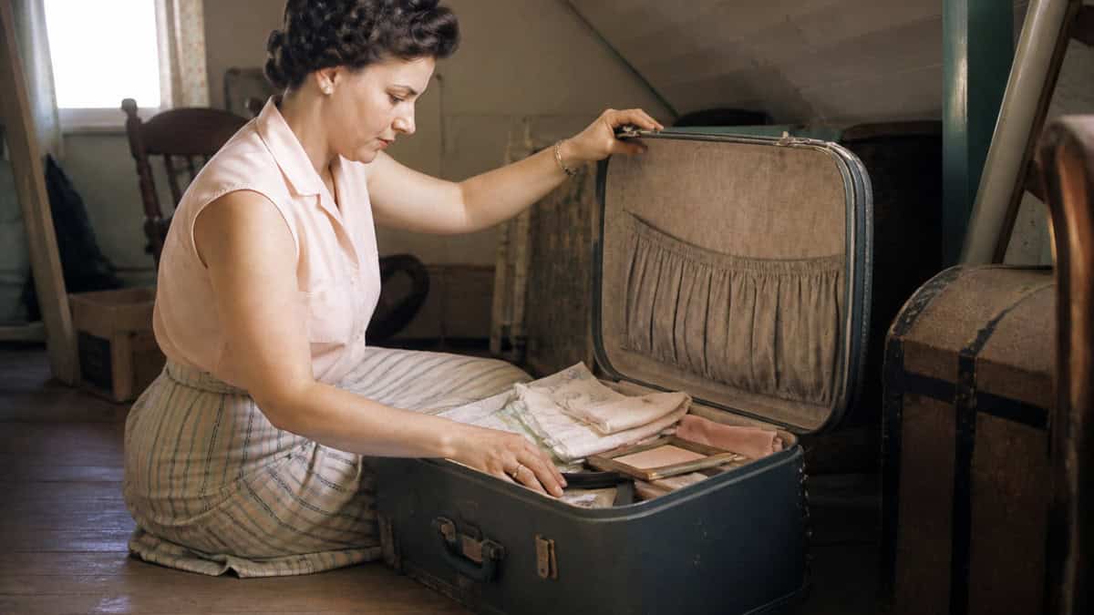 26 Things Grandma Never Threw Away (That Are Worth a Fortune Now) 14 Woman opening a saved hard-sided vintage suitcase in an early-1960s attic